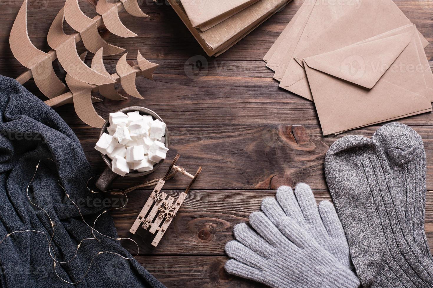 Winter still life. Marshmallow drink, warm clothes, craft envelopes and Christmas trees on a wooden photo