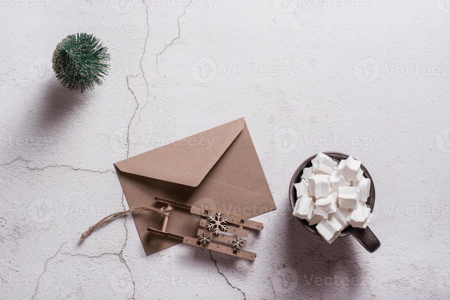 Cocoa with marshmallows, a craft envelope and a wooden sled on plaster. Top view. photo