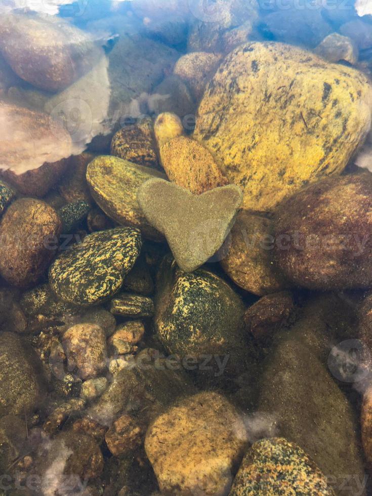 The heart-shaped stone lies at the bottom of the river, vertical orientation photo