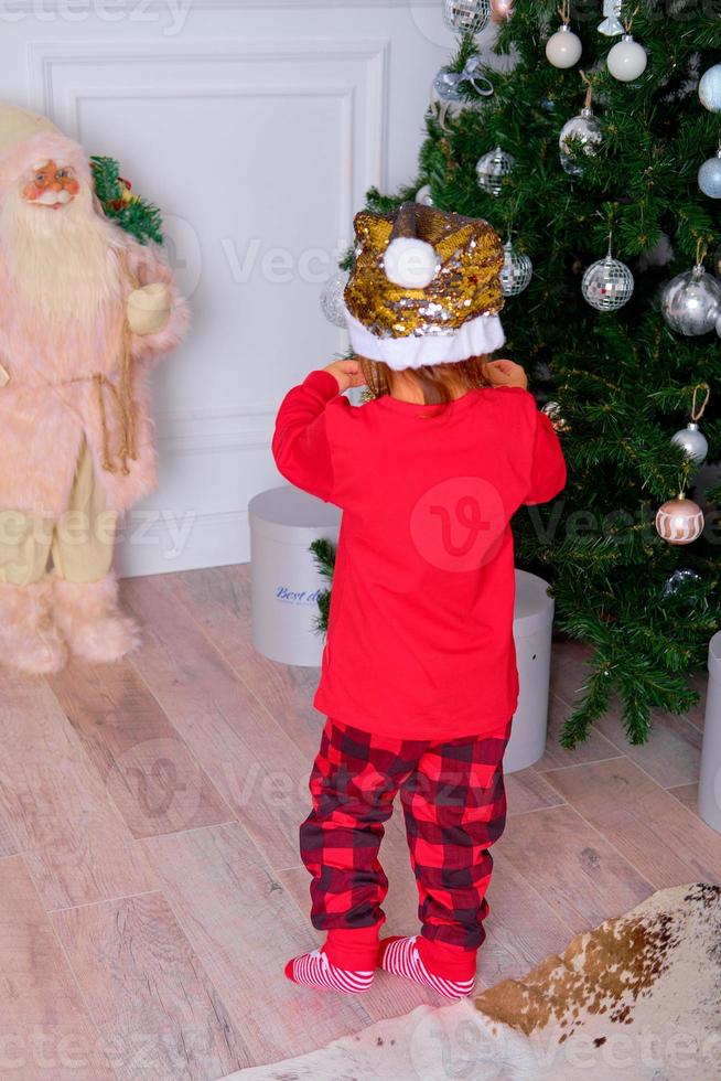 niña en lindo pijama decora un árbol de navidad foto