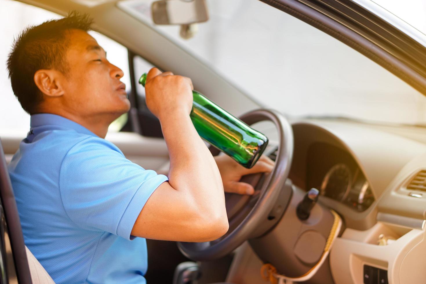 un borracho asiático sostiene una botella de cerveza para beber en el auto. concepto, deja de conducir mientras bebes alcohol o campaña de whisky. ilegal y peligroso conducir un vehículo que conduce a un accidente. foto