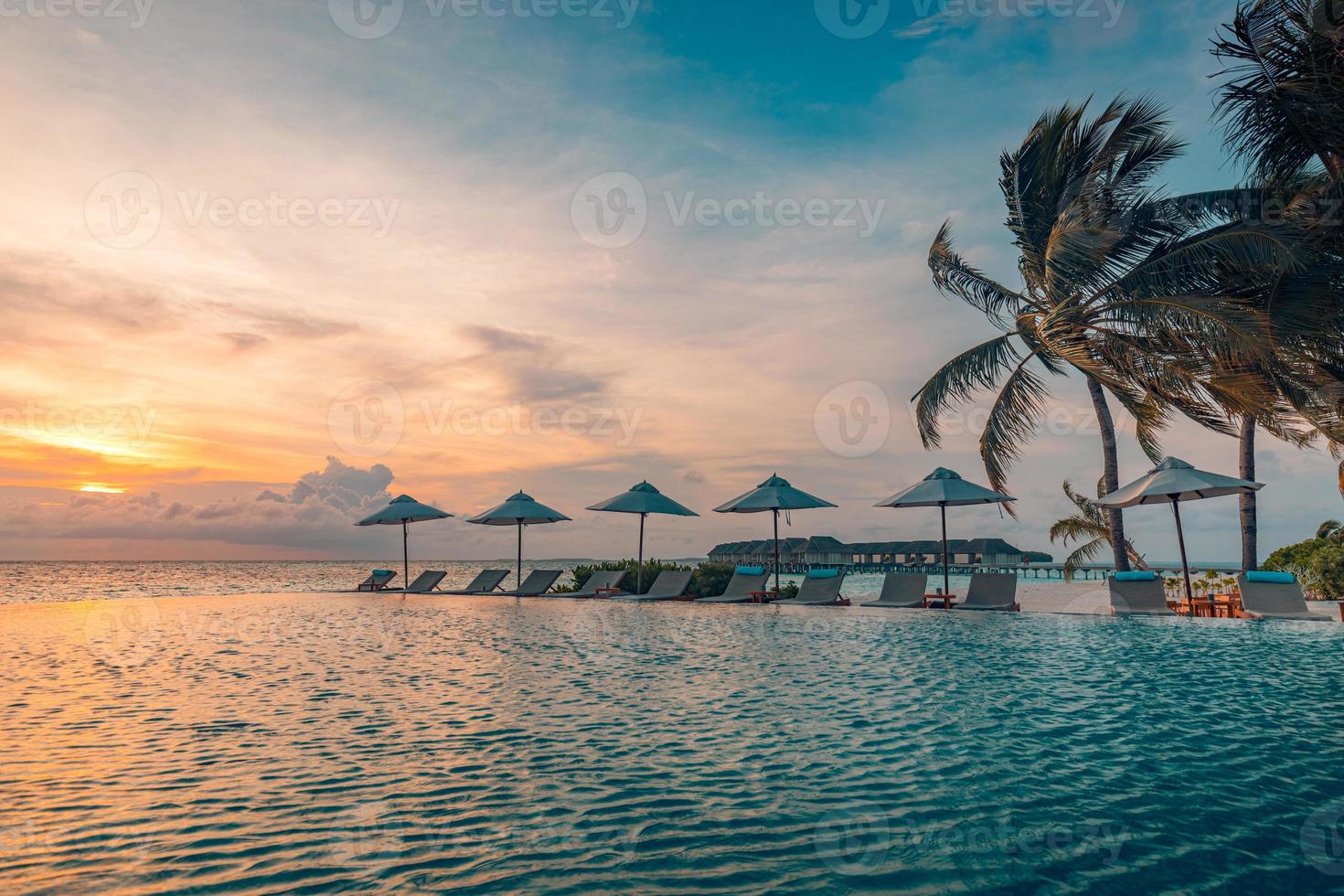 Outdoor luxury sunset over infinity pool swimming summer beachfront hotel resort, tropical landscape. Beautiful tranquil beach holiday vacation background. Amazing island sunset beach view, palm trees photo
