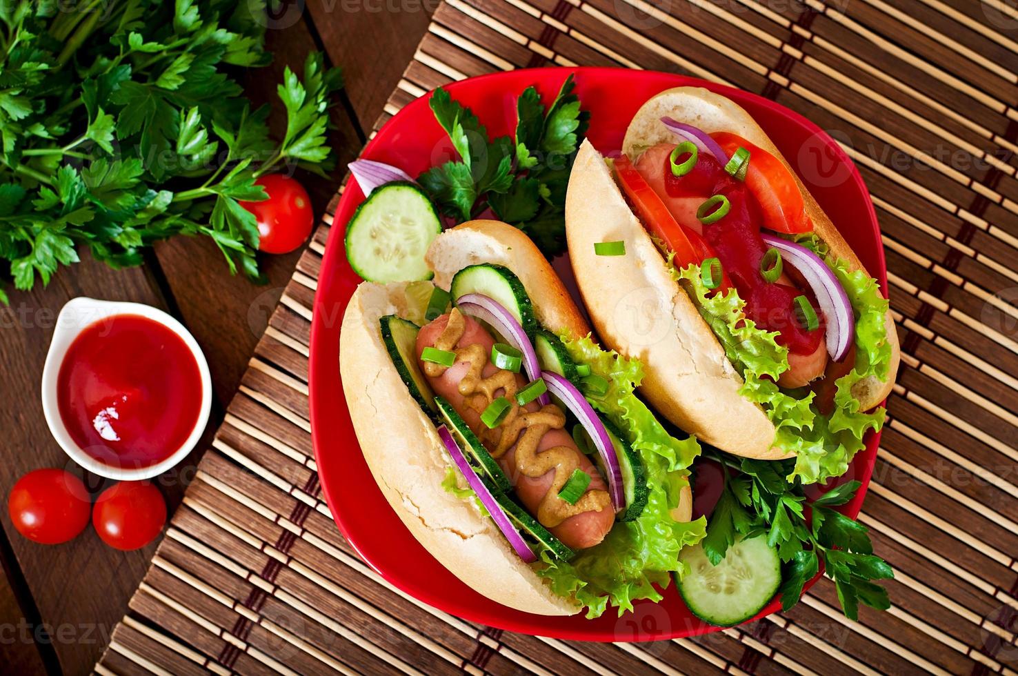 Hot Dog con salsa de tomate, mostaza, lechuga y verduras en la mesa de madera foto