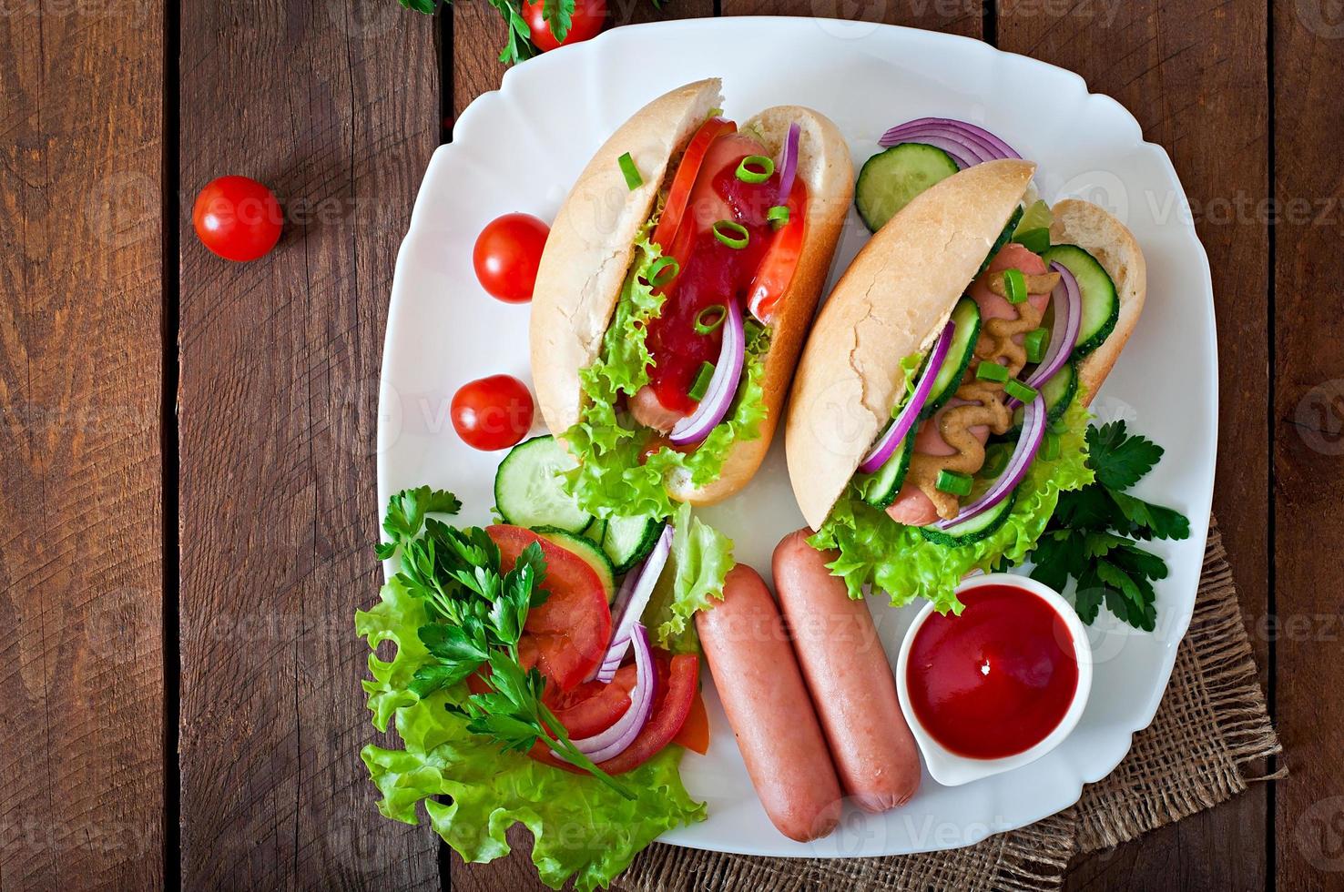 Hot Dog con salsa de tomate, mostaza, lechuga y verduras en la mesa de madera foto