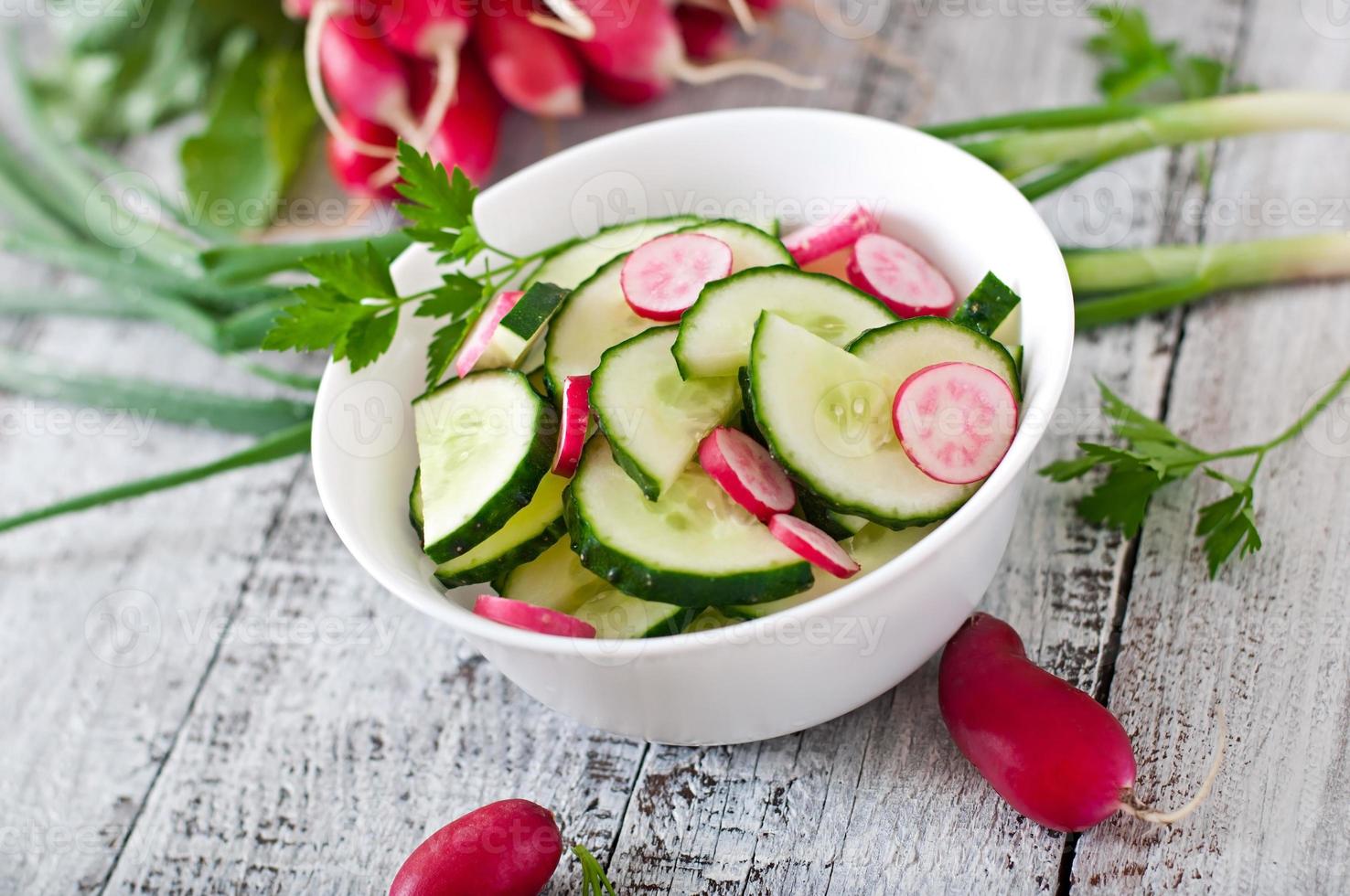 Fresh salad of cucumbers and radishes in a white bowl on the old wooden background photo