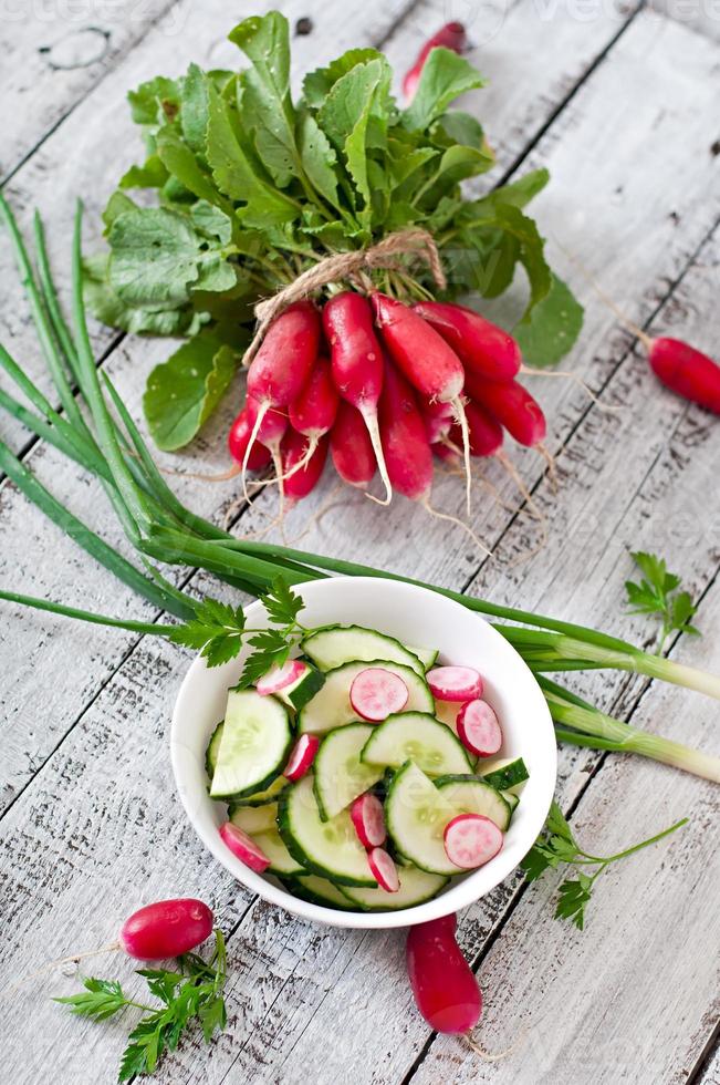 Fresh salad of cucumbers and radishes in a white bowl on the old wooden background photo