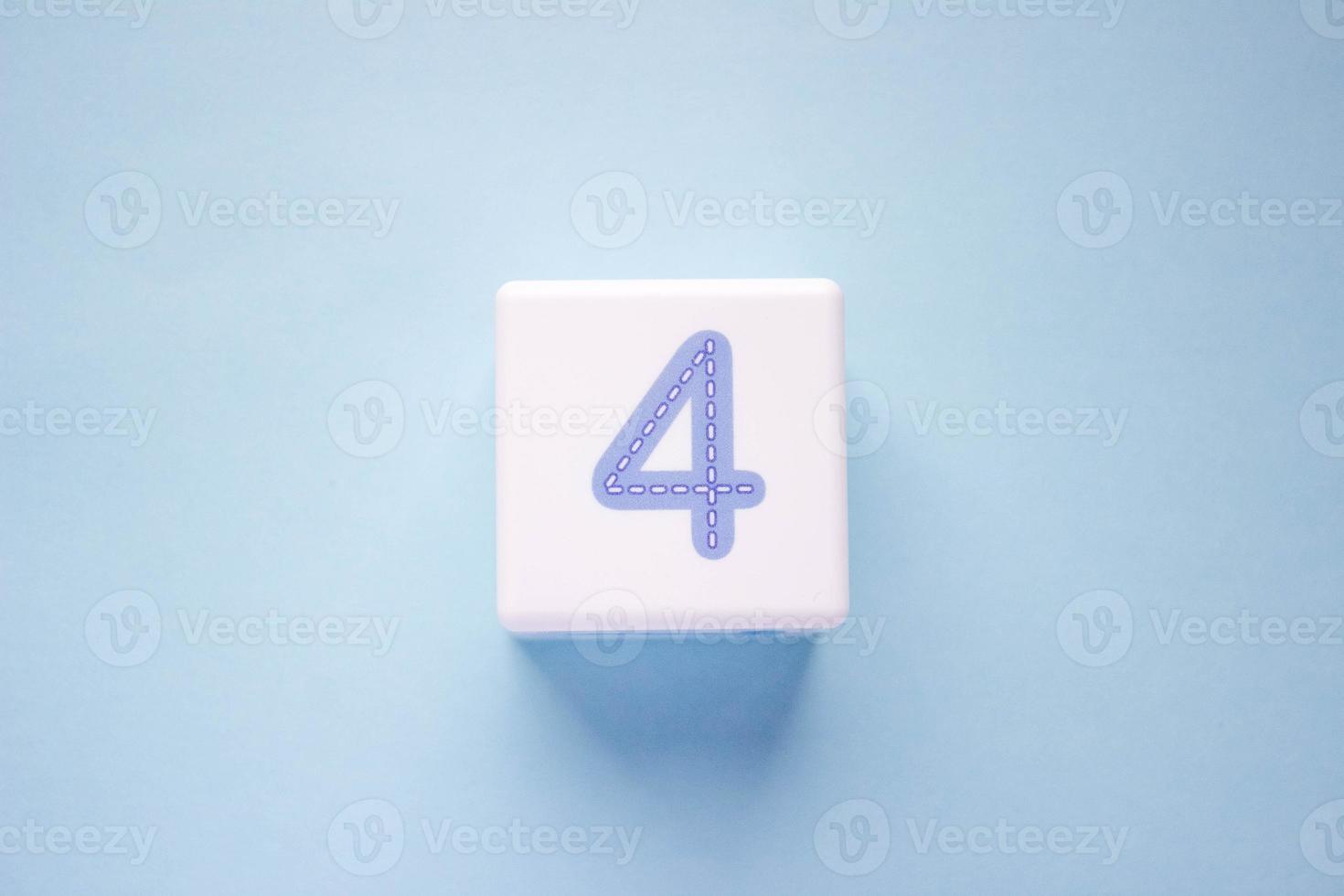 Close-up photo of a white plastic cube with a blue number 4 on a blue background. Object in the center of the photo