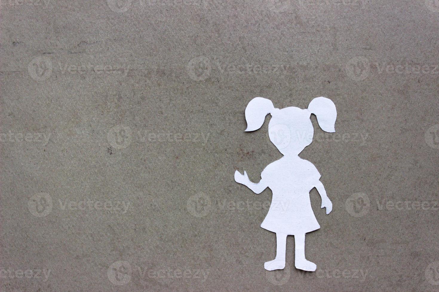 Silhouette of a girl in a dress and with ponytails made of white paper, cut by hand. In the right side of the photo. On beige background with copy space photo