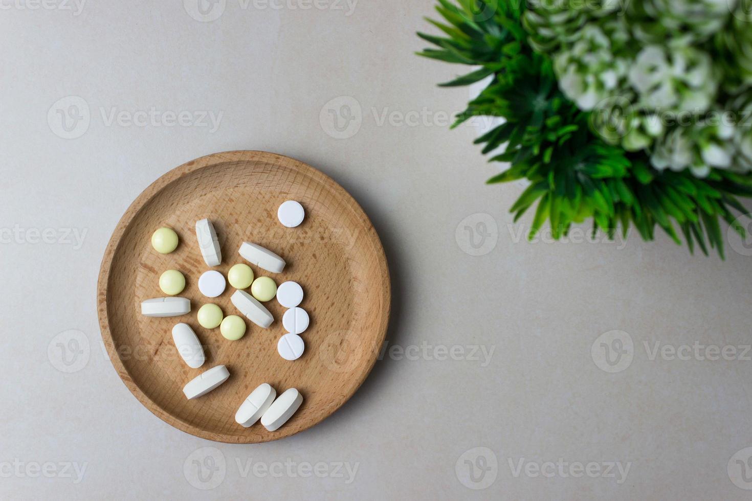 un puñado de pastillas en un plato de madera con planta verde. el concepto de medicina, tratamiento. vista superior. foto