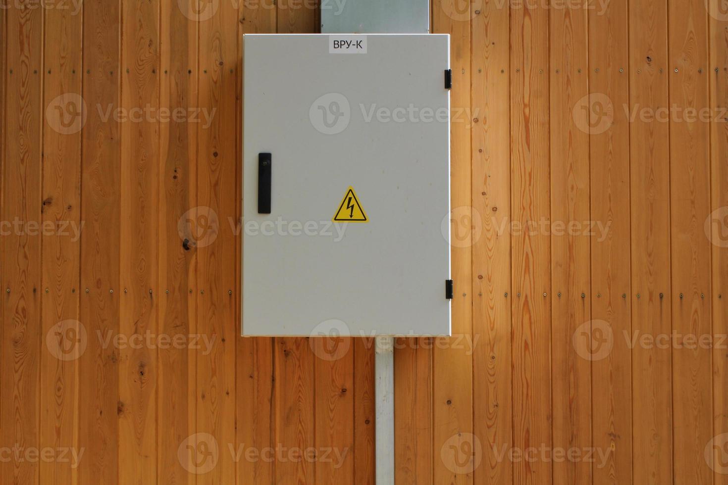 Knife switch and high voltage hazard sign on the wooden wall of house. Yellow electrical warning danger triangle symbol and metal security fence box. Closed lock electric panel transformer substation photo