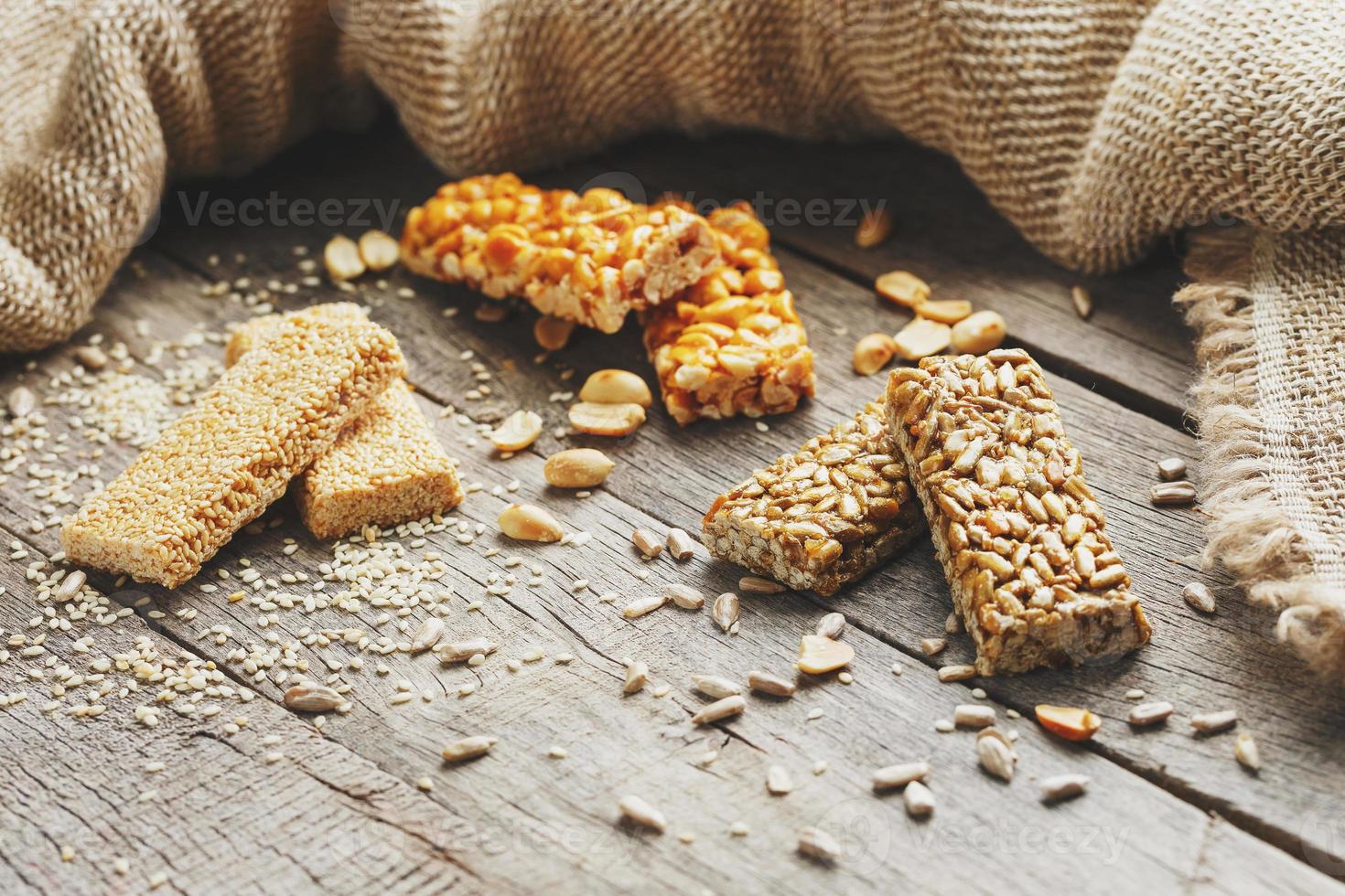 mezcla de gozinaki barra de semillas sobre un fondo vintage con arpillera. deliciosos dulces orientales a base de semillas de girasol, sésamo y maní, cubiertos de miel con glaseado brillante. estilo macro campestre foto