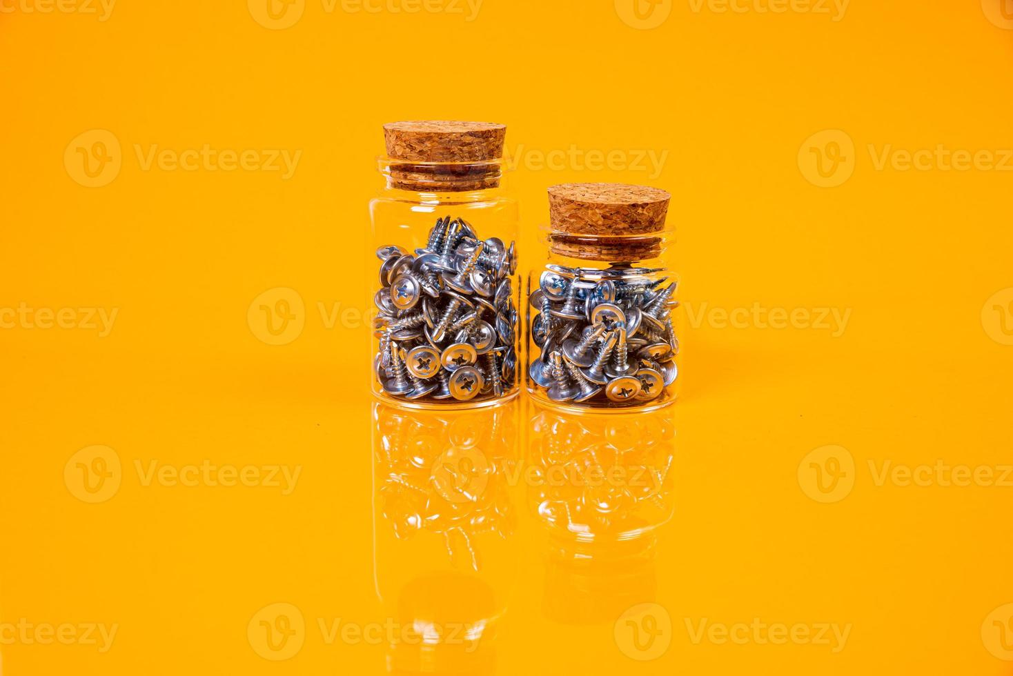 Many metal self-tapping screws made of steel in a glass, in bucket jar. self-tapping screw for metal, for iron, chrome-plated self-tapping screw, on an orange yellow background, photo
