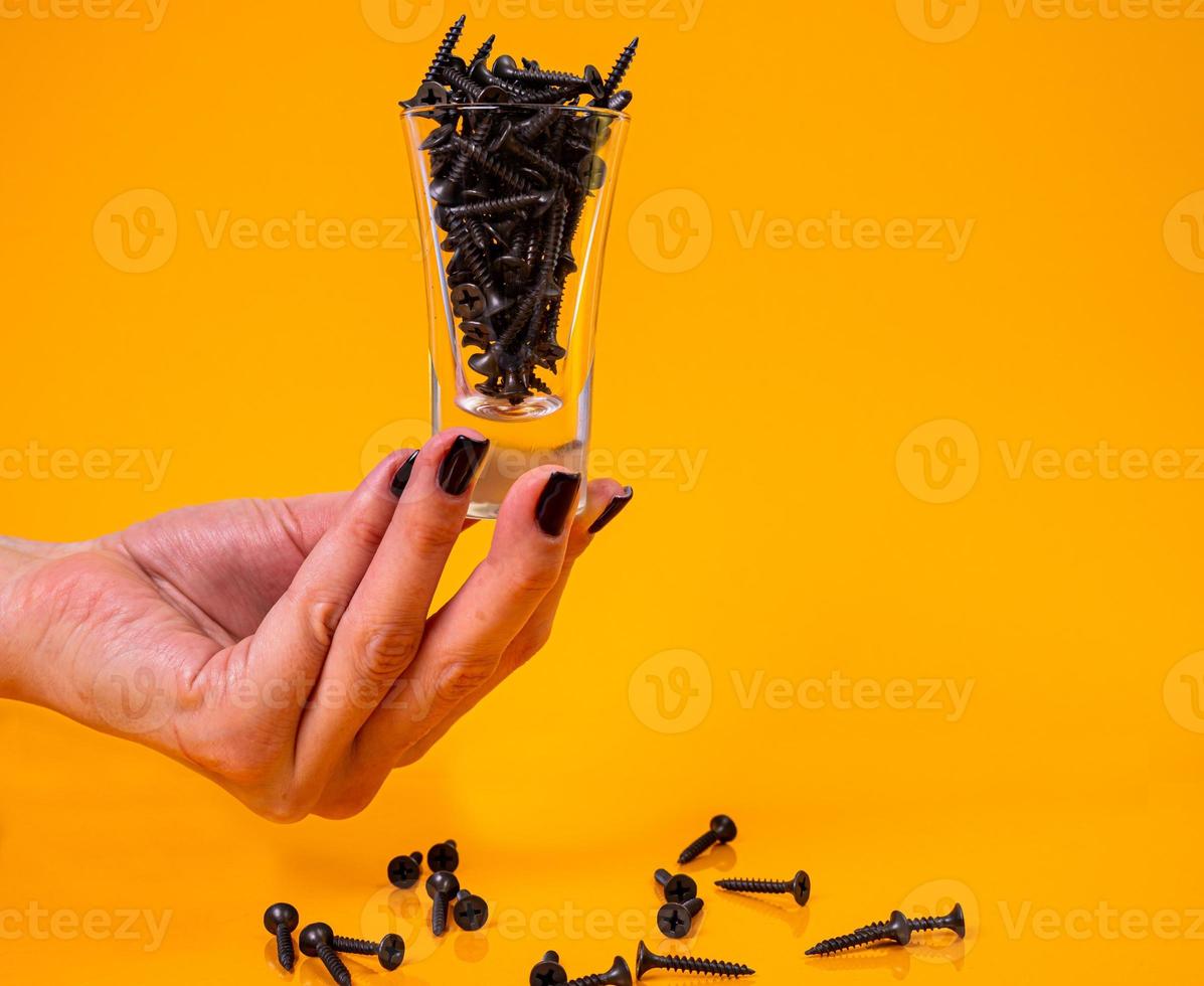 Dropped Many metal self-tapping screws made of steel in a glass, in bucket jar. self-tapping screw for metal, for iron, chrome-plated self-tapping screw, on an orange yellow background, photo