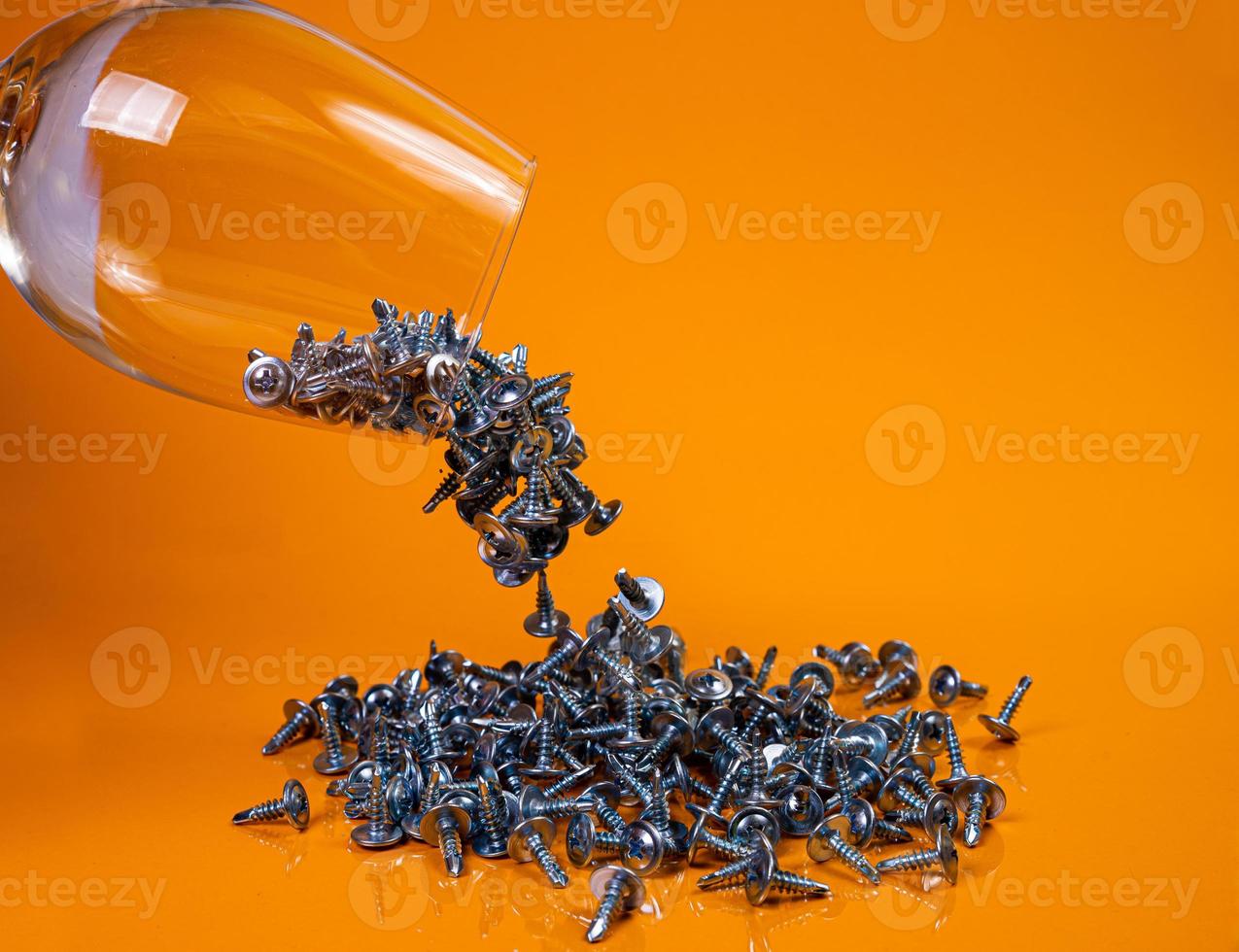 Dropped Many metal self-tapping screws made of steel in a glass, in bucket jar. self-tapping screw for metal, for iron, chrome-plated self-tapping screw, on an orange yellow background, photo