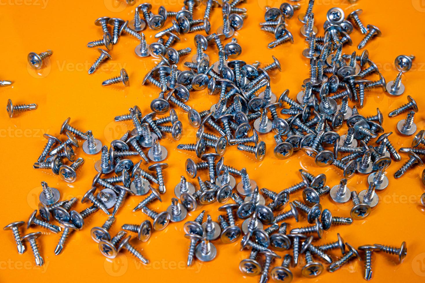 Many metal self-tapping screws made of steel in a glass, in bucket jar. self-tapping screw for metal, for iron, chrome-plated self-tapping screw, on an orange yellow background, photo