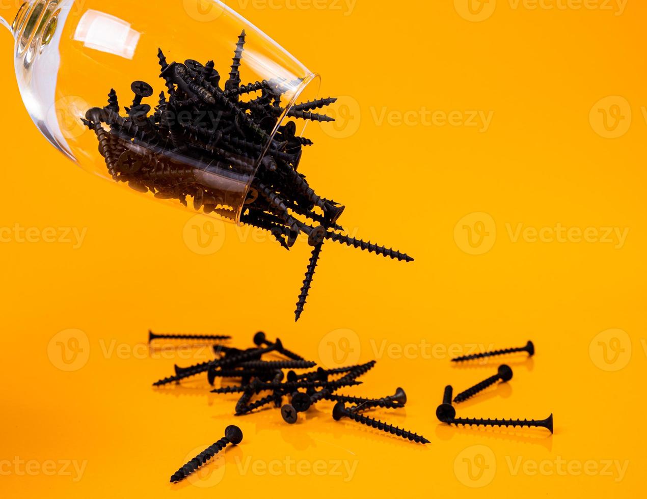 Dropped Many metal self-tapping screws made of steel in a glass, in bucket jar. self-tapping screw for metal, for iron, chrome-plated self-tapping screw, on an orange yellow background, photo