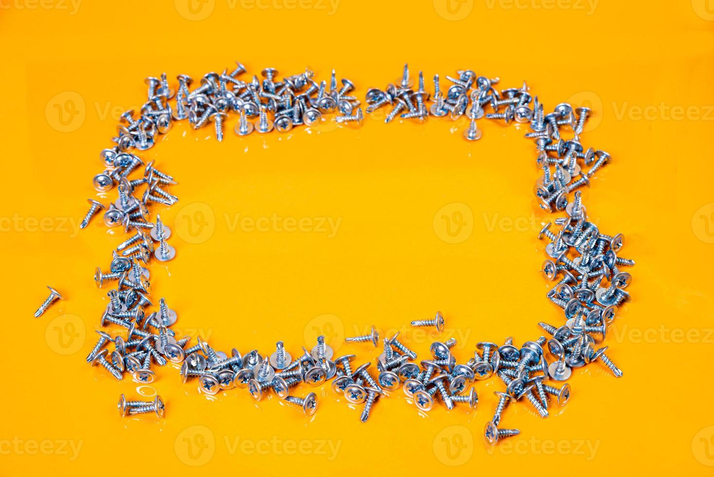 Many metal self-tapping screws made of steel in a glass, in bucket jar. self-tapping screw for metal, for iron, chrome-plated self-tapping screw, on an orange yellow background, photo