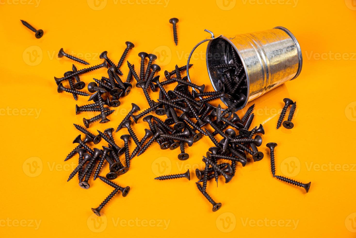 Many metal self-tapping screws made of steel in a glass, in bucket jar. self-tapping screw for metal, for iron, chrome-plated self-tapping screw, on an orange yellow background, photo