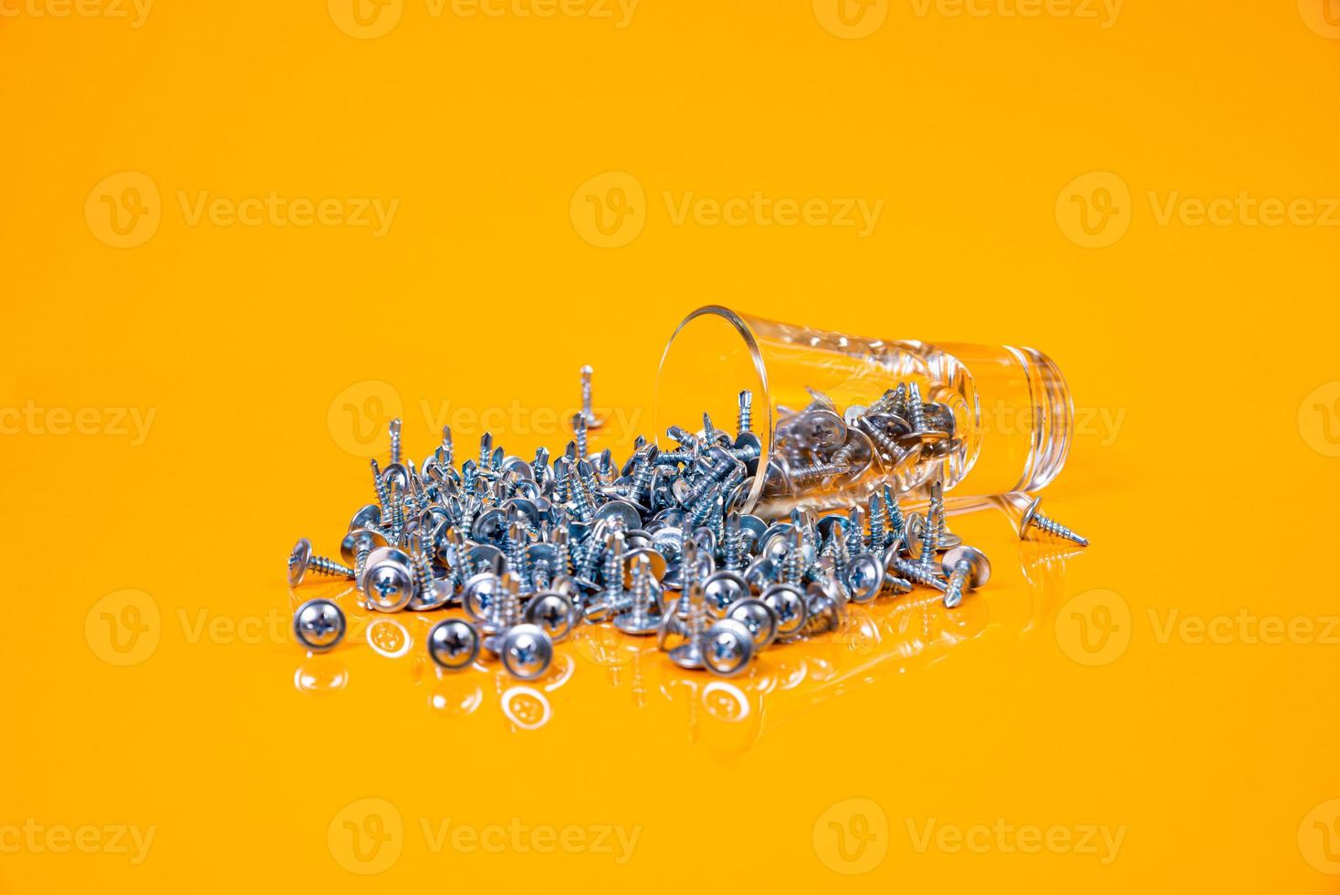 Many metal self-tapping screws made of steel in a glass, in bucket jar. self-tapping screw for metal, for iron, chrome-plated self-tapping screw, on an orange yellow background, photo