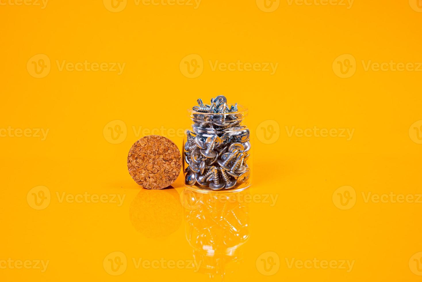 Many metal self-tapping screws made of steel in a glass, in bucket jar. self-tapping screw for metal, for iron, chrome-plated self-tapping screw, on an orange yellow background, photo