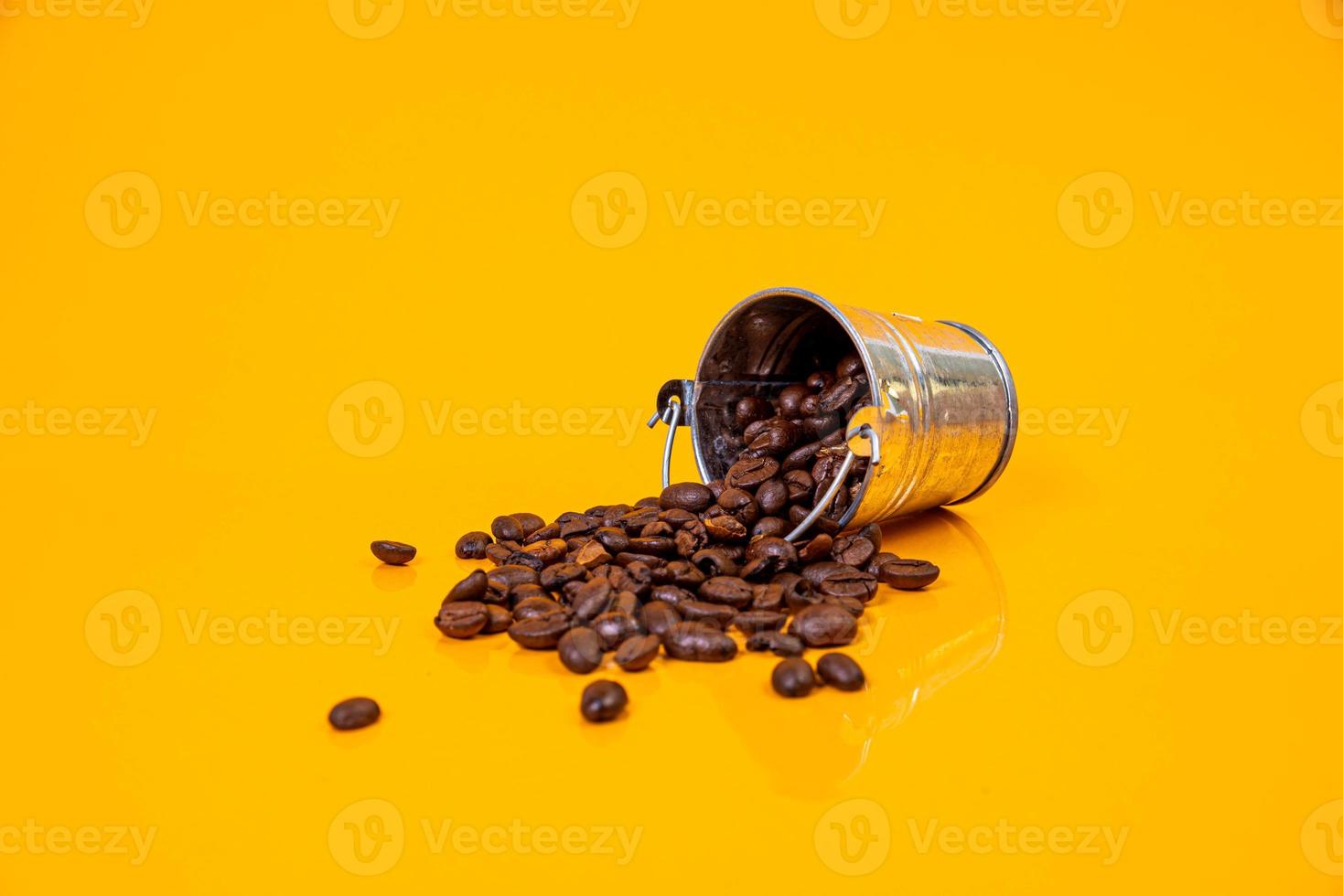 Dropped Many roasted coffee beans in a glass, in bucket jar. self-tapping screw for metal, for iron, chrome-plated self-tapping screw, orange yellow background photo