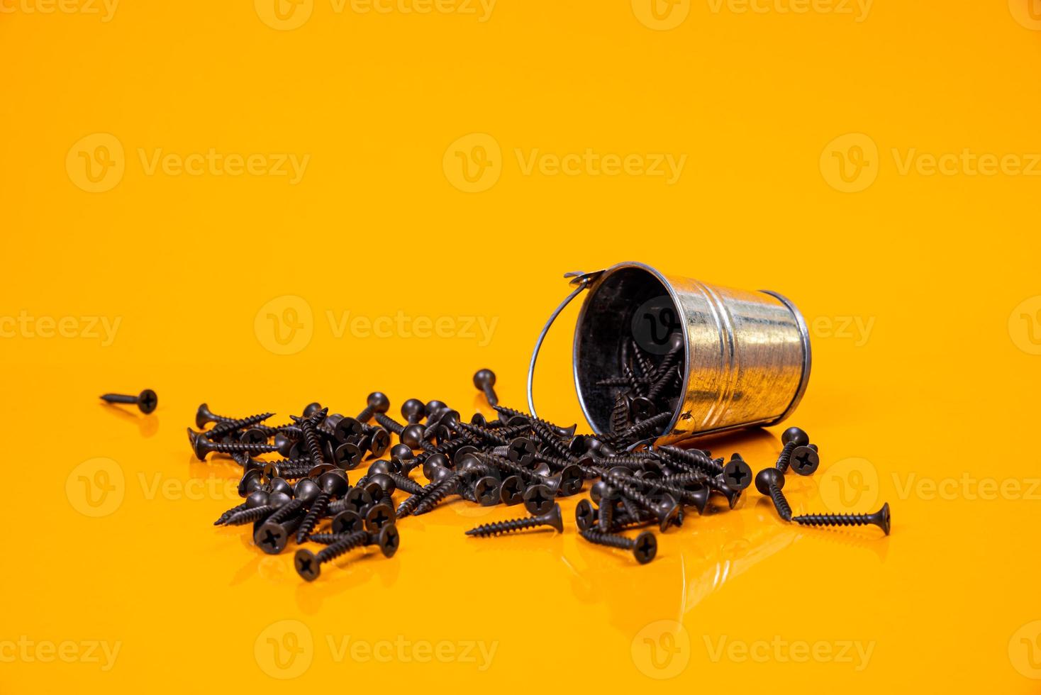 Many metal self-tapping screws made of steel in a glass, in bucket jar. self-tapping screw for metal, for iron, chrome-plated self-tapping screw, on an orange yellow background, photo