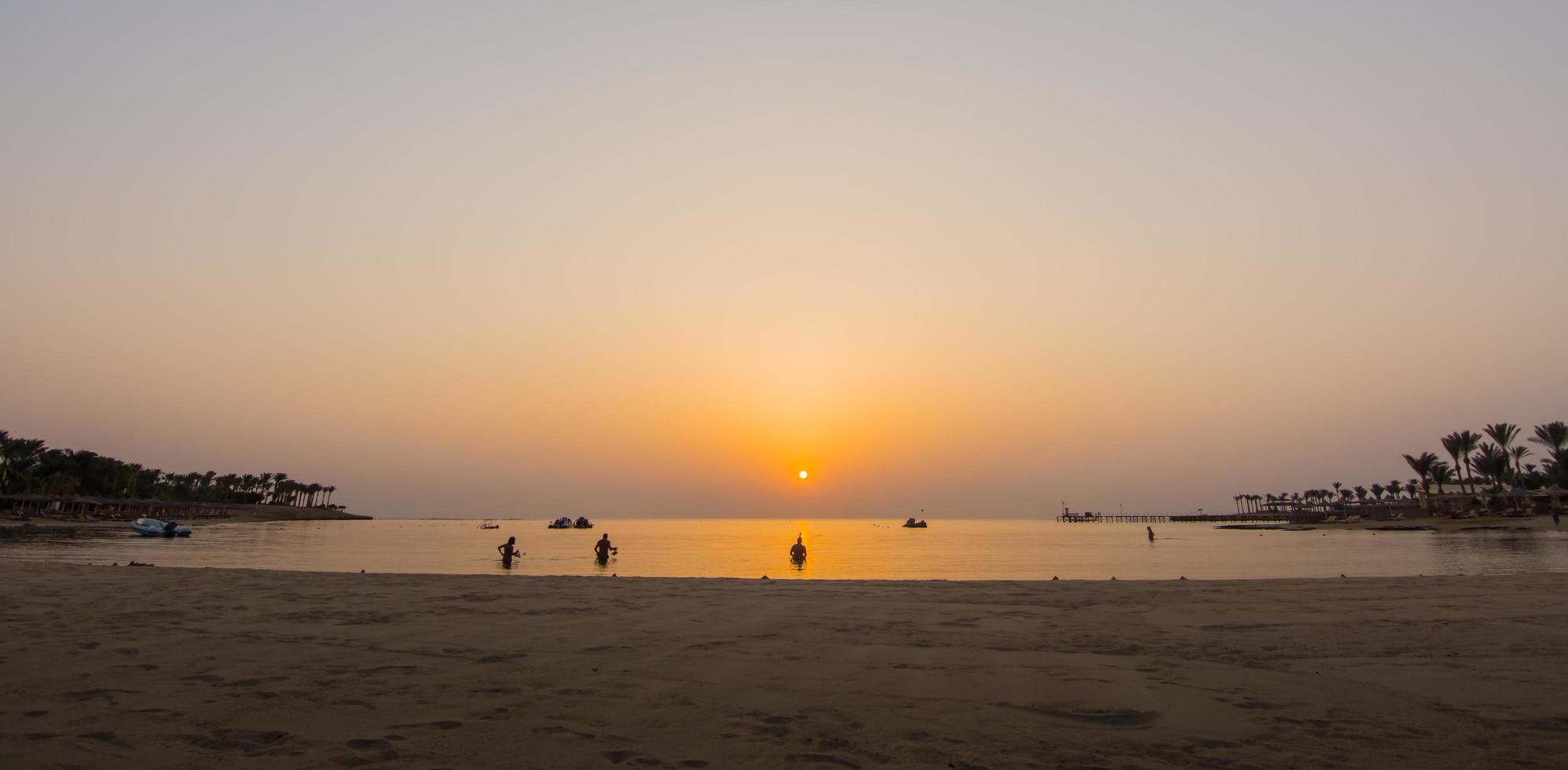 cálido sol naranja al amanecer con buceadores en la playa en el panorama de Egipto foto