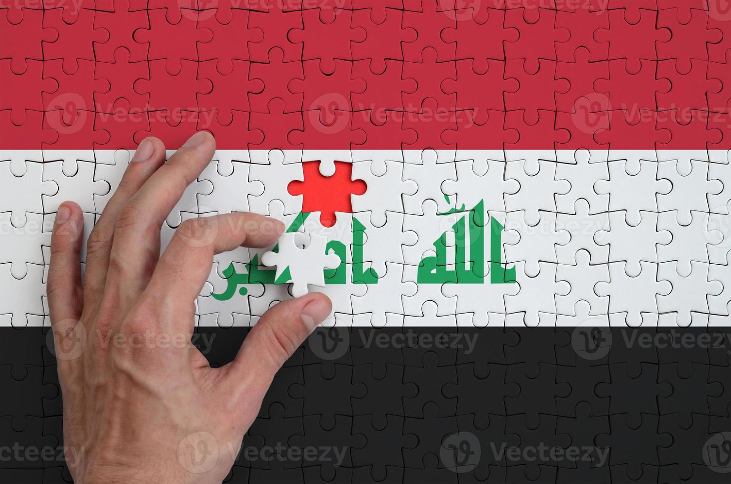 Iraq flag is depicted on a puzzle, which the man's hand completes to fold photo