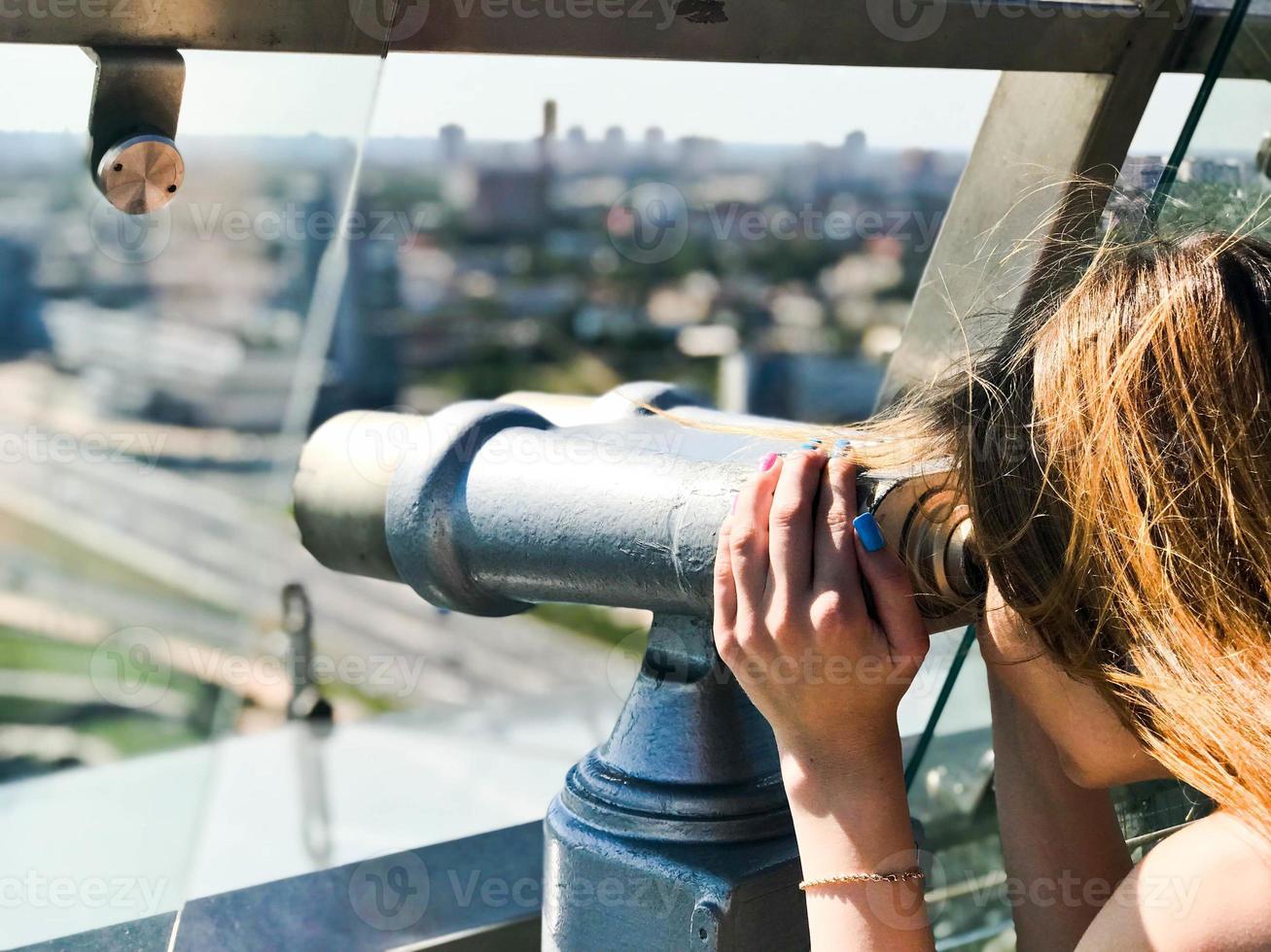A beautiful girl looks at the landscape, a panorama of the city in the observation room, a pair of binoculars, a telescope with a bill acceptor on an observation deck in the open air photo