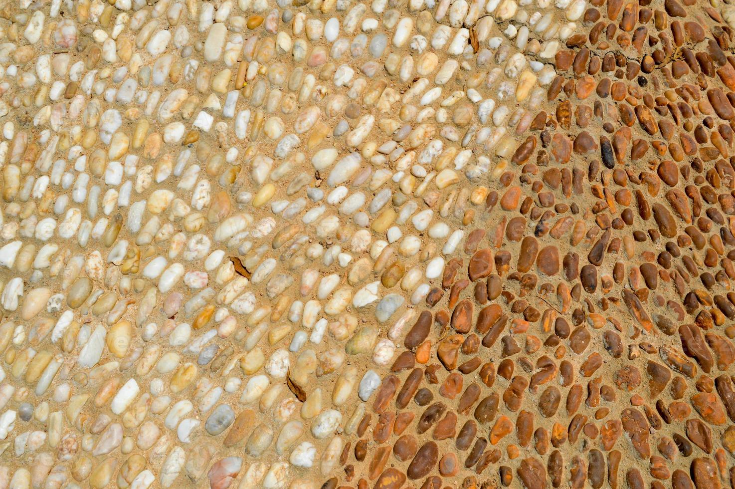 The texture of the stone wall, the road from small round and oval stones with abstract lines laid out patterns with two-color sandy seams of natural old yellow black brown. The background photo