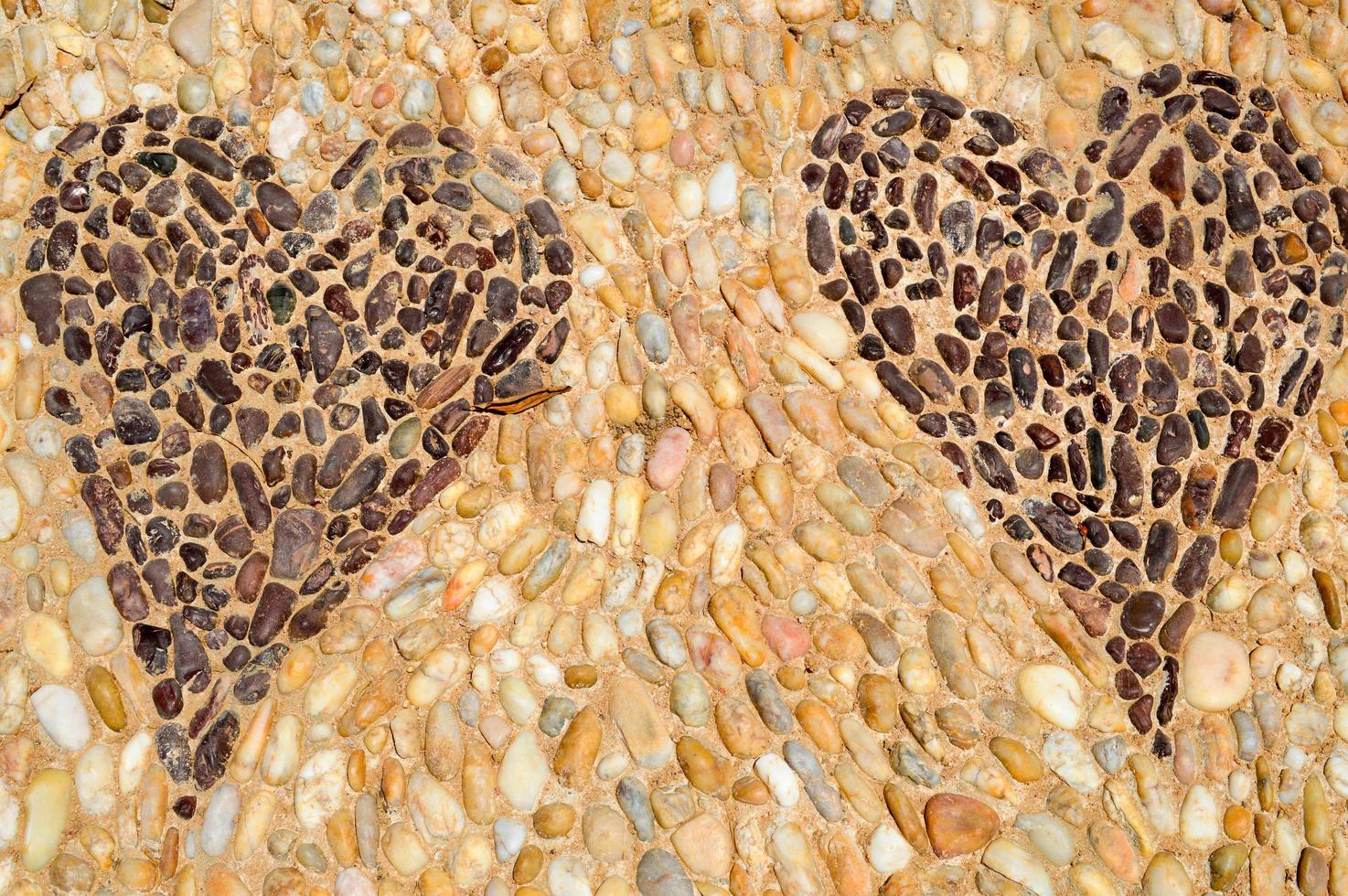 la textura de la pared de piedra, el camino de pequeñas piedras redondas y ovaladas con líneas abstractas de patrones de dos corazones, costuras arenosas de marrón amarillo negro antiguo natural. el fondo foto