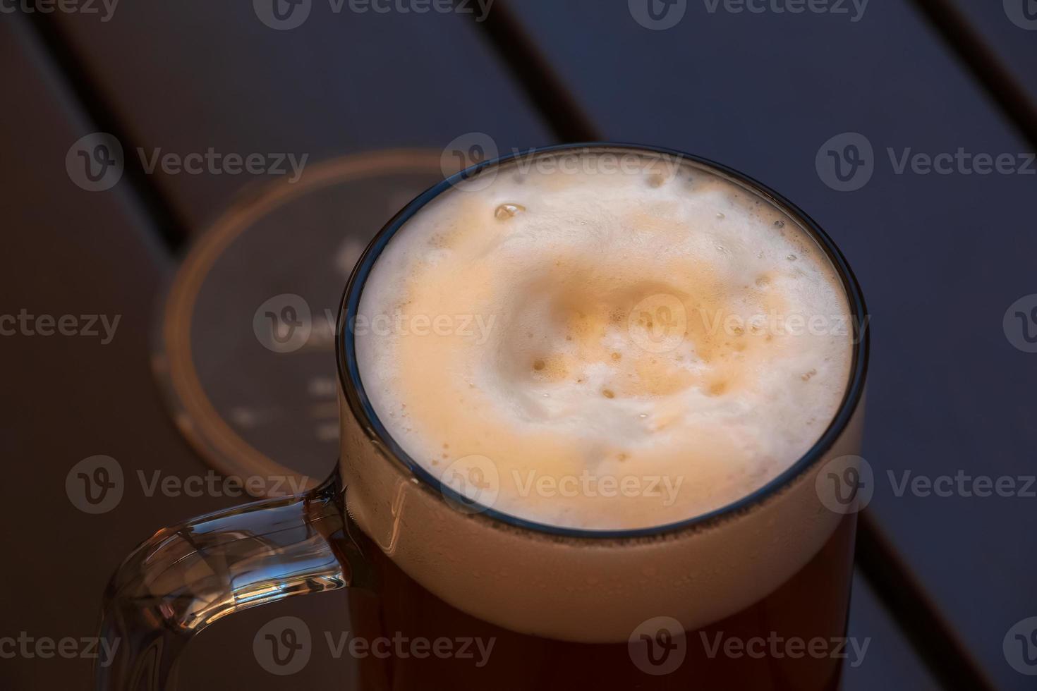 Mug of beer with white dense foam on a wooden background. photo