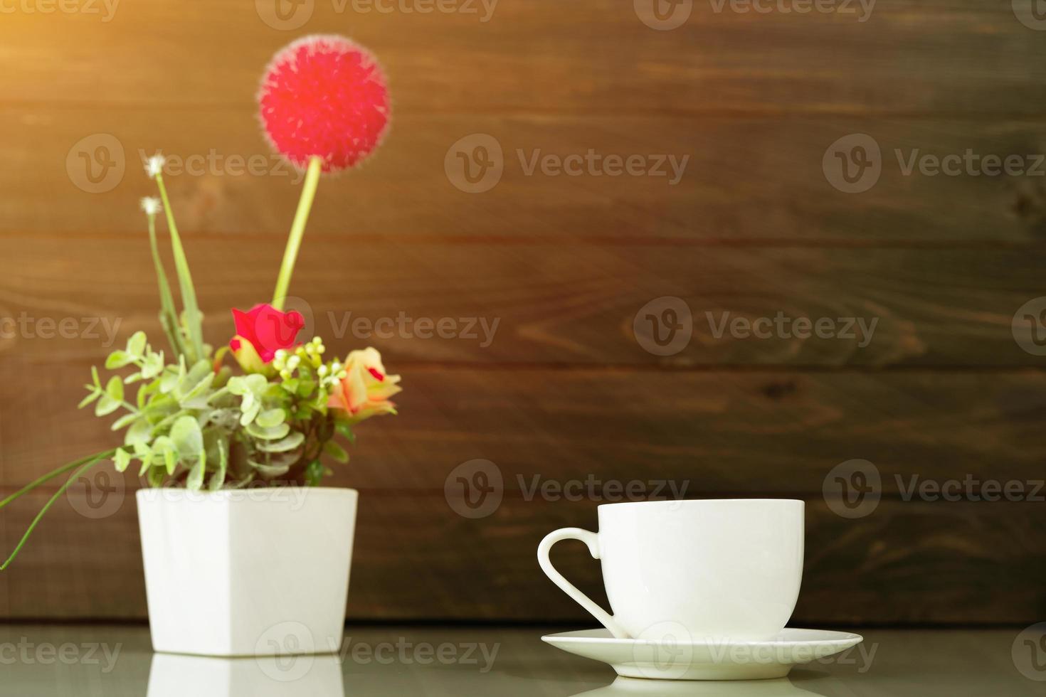 Coffee cup and Artificial flower vase bouquet over table photo