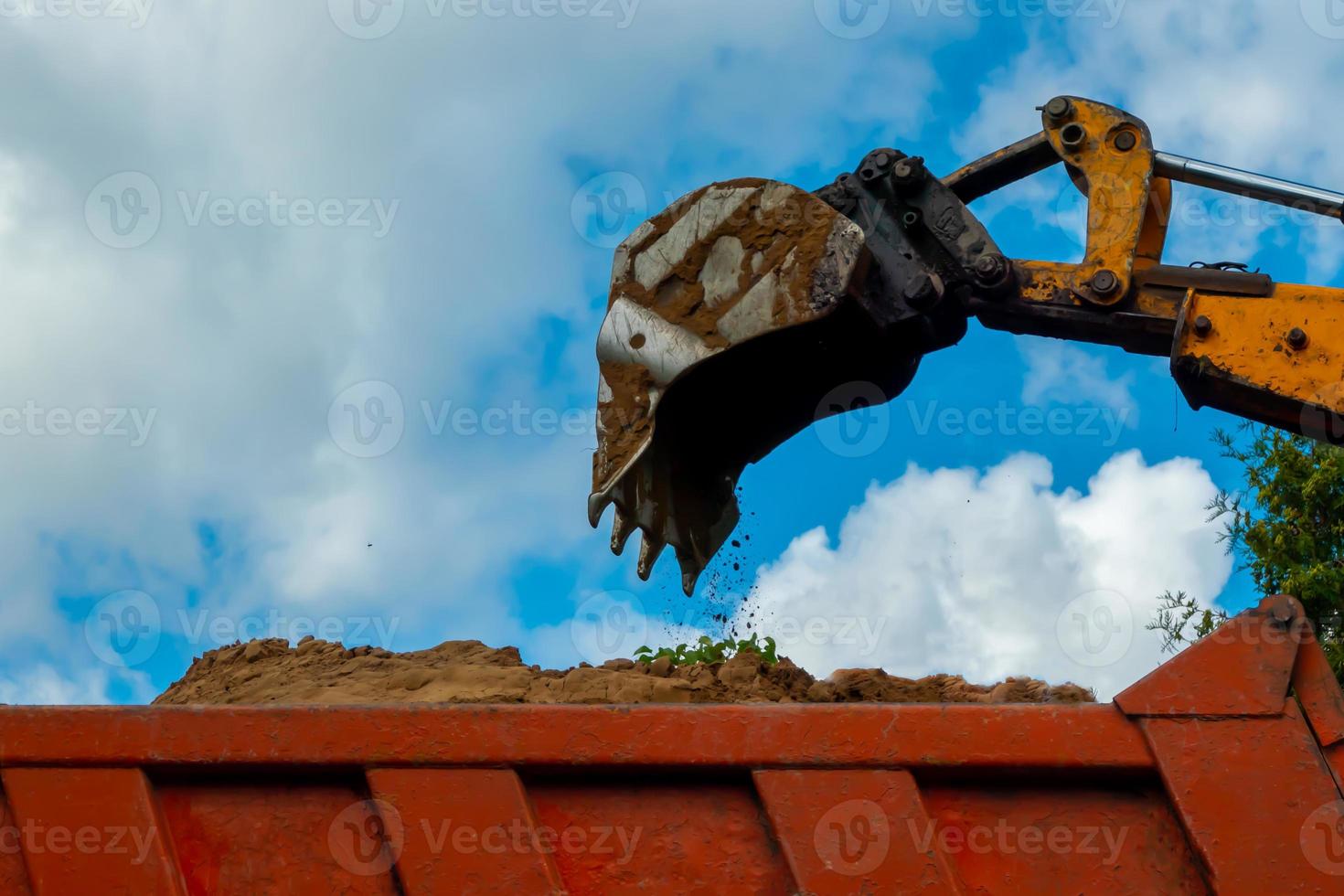 Orange excavator unloads sand from a dump truck. Dig in the agricultural area. photo