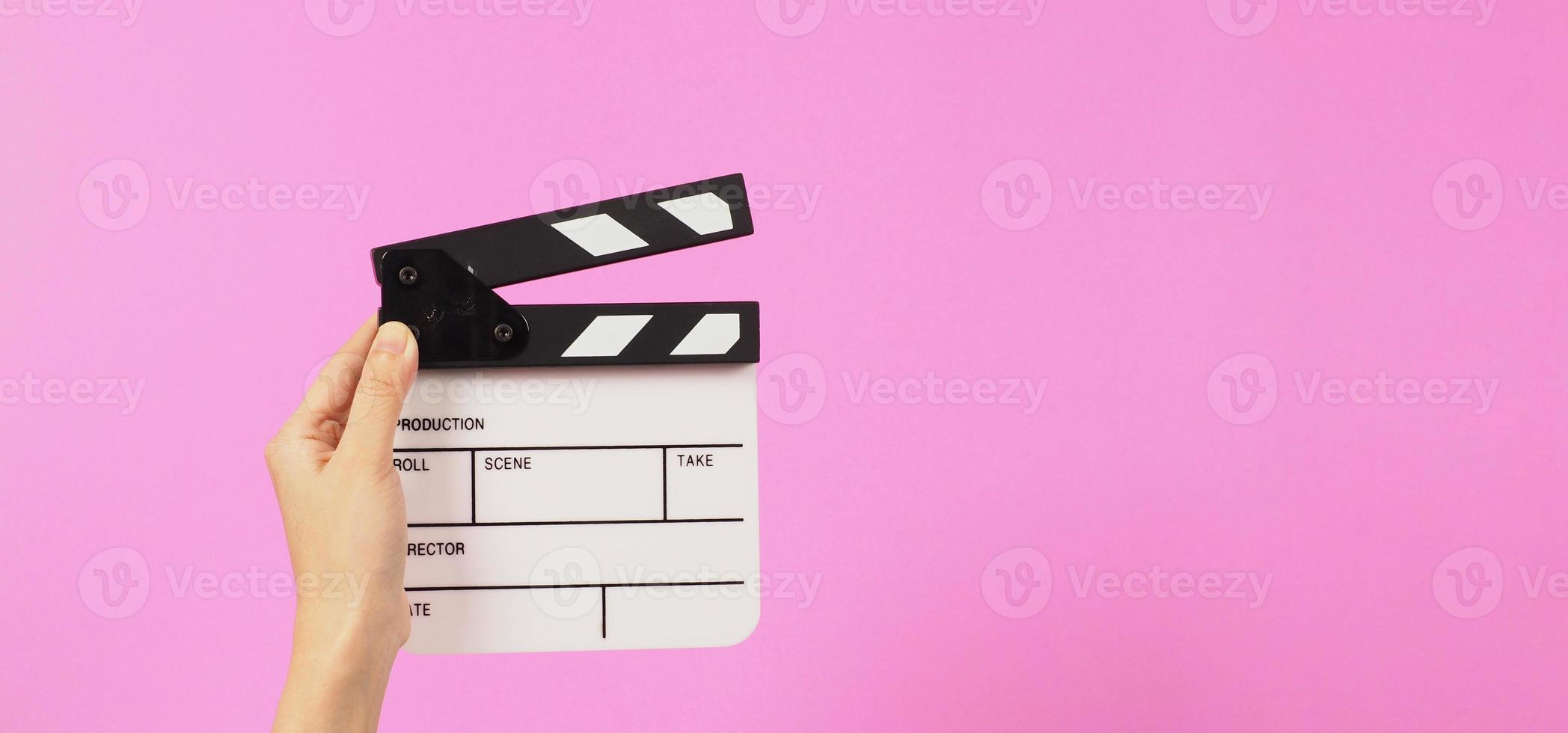 Top eye view. The hand is holding a small white clapper board or movie slate on pink background. photo