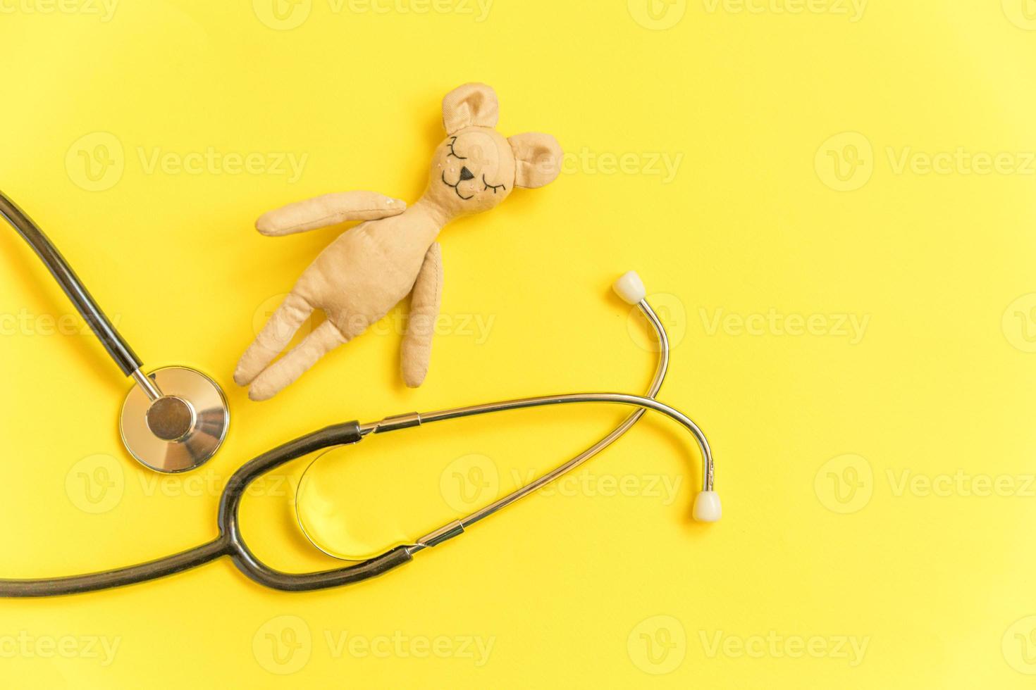 estetoscopio de equipo de medicina y oso de juguete de diseño simplemente mínimo aislado sobre fondo amarillo. concepto de médico de niños de atención médica. símbolo de pediatra. diseño de vista superior plana, espacio de copia foto