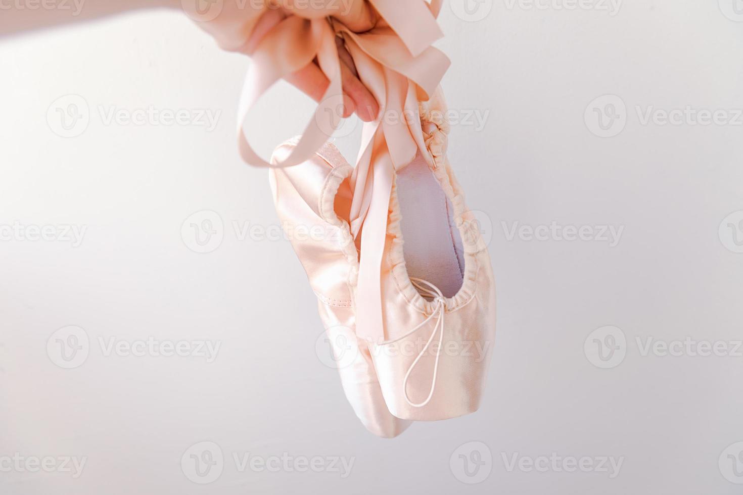 Ballerina dancer hand holding new pastel beige ballet shoes with satin ribbon isolated on white background. Ballerina classical pointe shoes for dance training. Ballet school concept. Copy space. photo