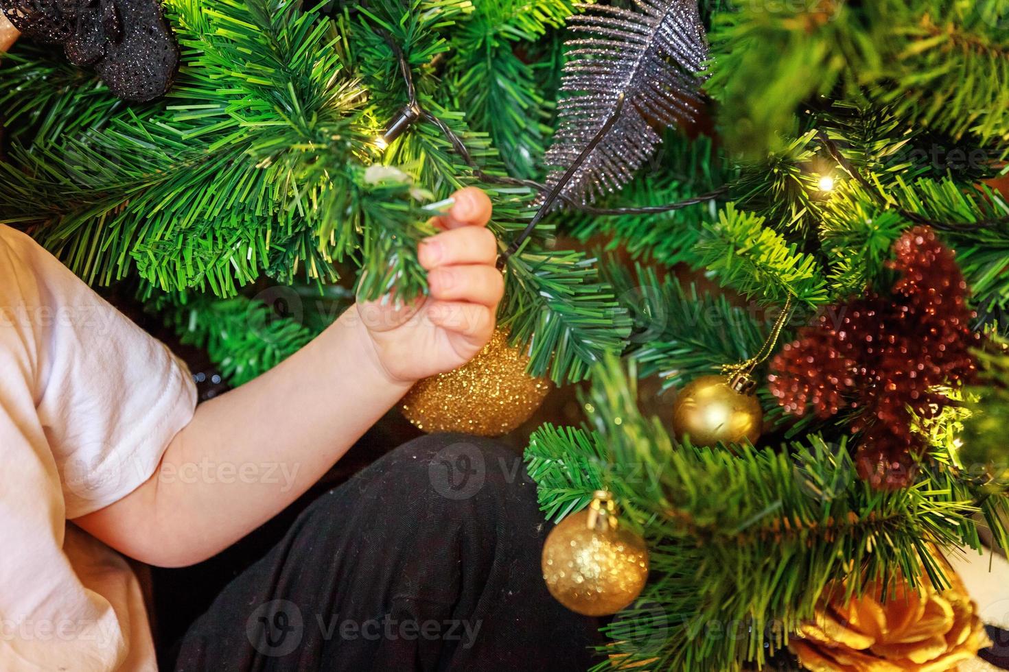 Close up baby hands decorating Christmas tree on Christmas eve at home. Young kid with winter decoration. Happy family at home. Christmas New Year december time for celebration concept. photo