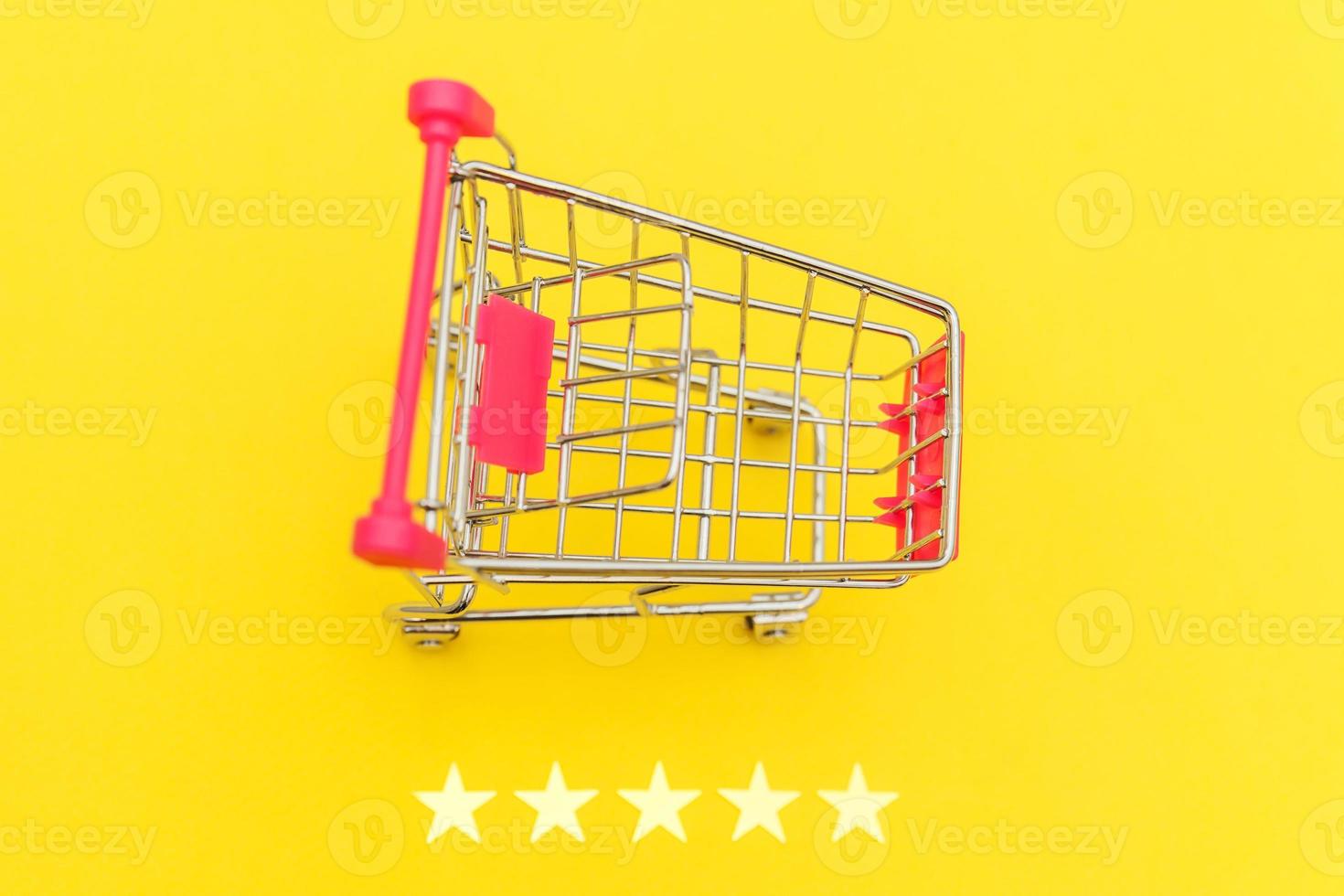 Small supermarket grocery push cart for shopping toy with wheels and 5 stars rating isolated on yellow background. Retail consumer buying online assessment and review concept. photo