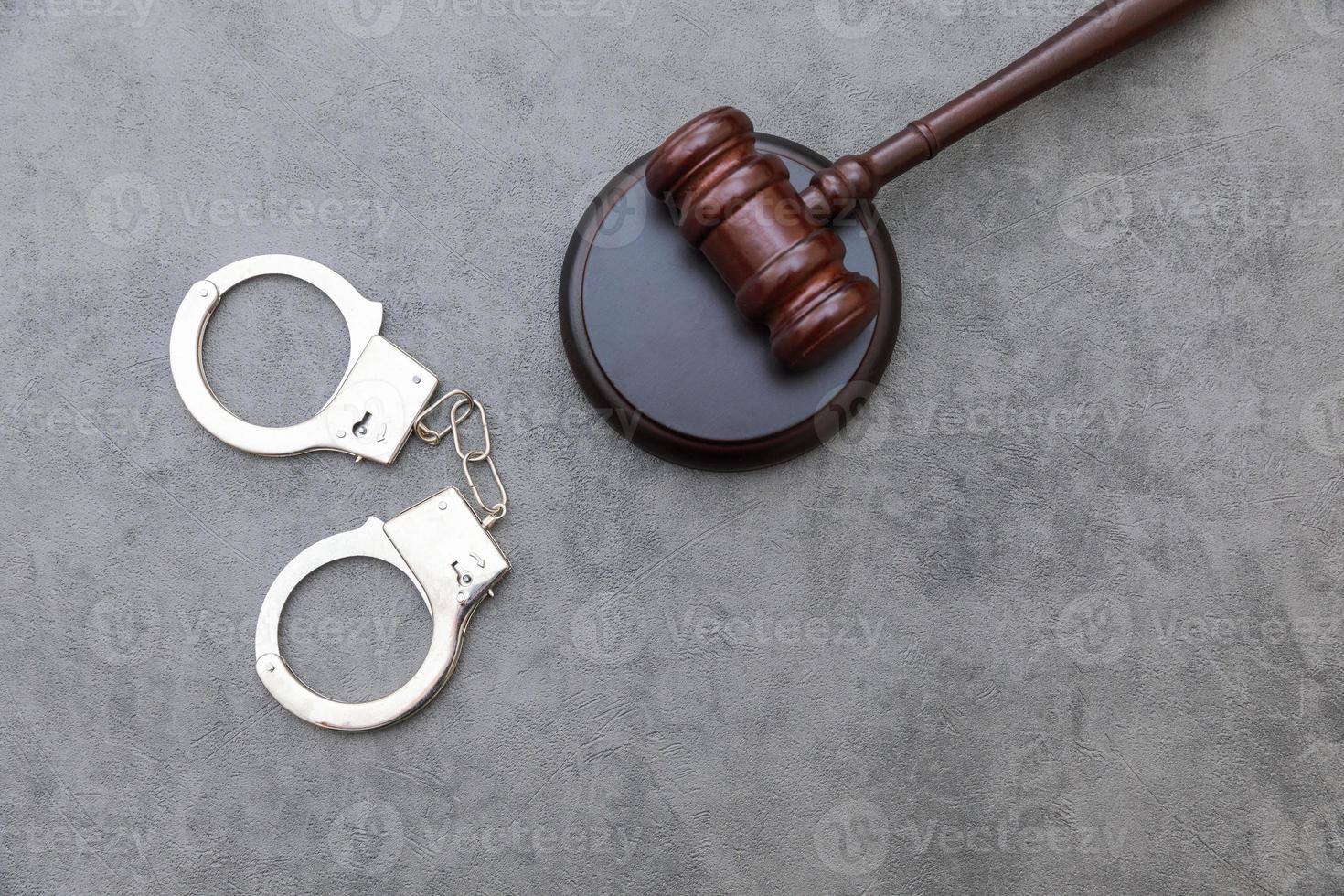 Law theme. Court of law trial in session. Judge gavel handcuffs on grey table in lawyer office or court session. Mallet of judge on concrete stone grey background. Justice human rights concept. photo