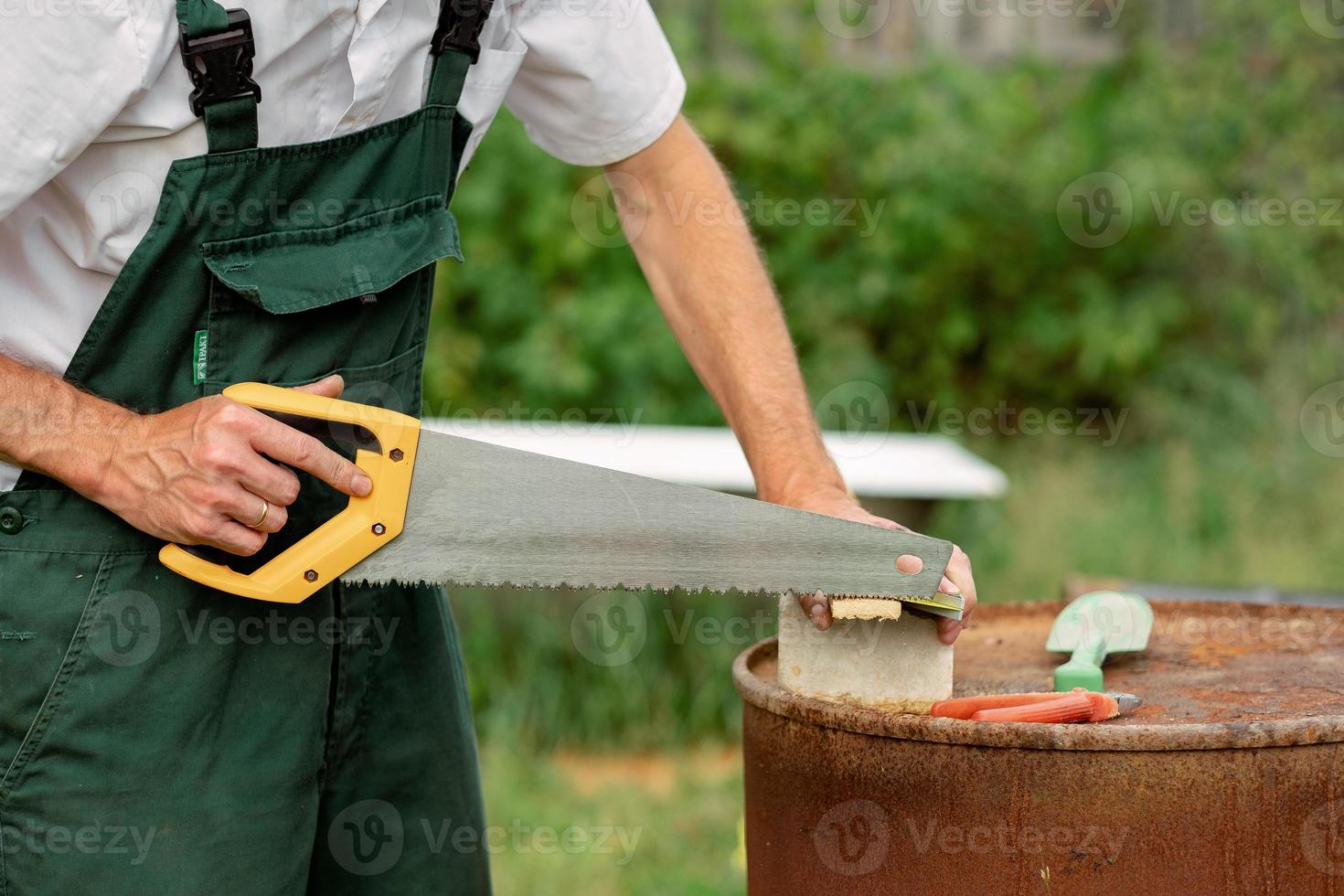 carpintero usando una sierra de madera para cortar láminas de madera. un carpintero con una sierra manual cortando una tabla de madera en un taller. carpintero a mano con una sierra con herramientas de seguridad. foto