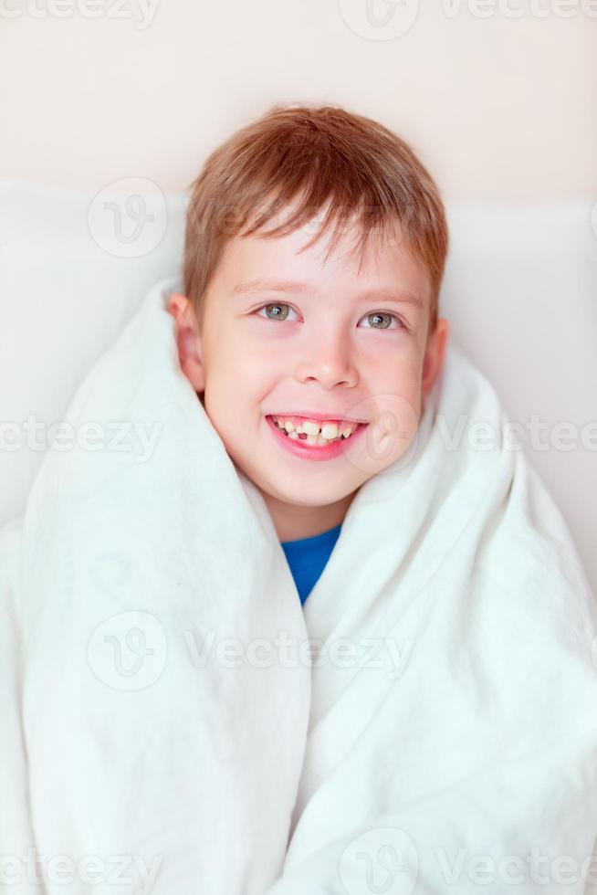 niño pequeño envuelto en una manta sobre fondo blanco. retrato de un niño sonriente. niño con una sonrisa desdentada. dientes blancos de un niño. bebé en una manta foto