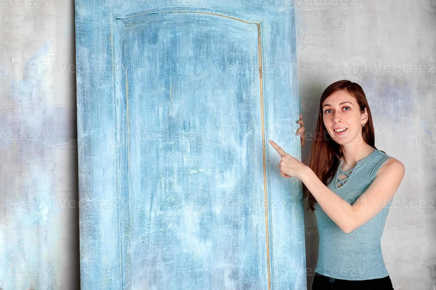 young brunette smiles and points a finger at a sign on a blue door photo