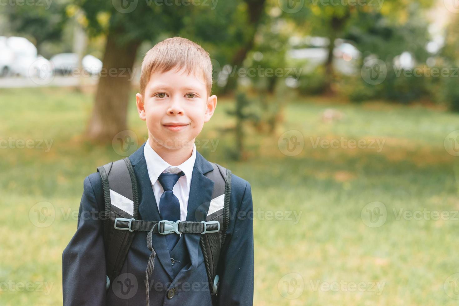 a schoolboy in a school uniform and a backpack stands on the street. Boy in school uniform. back to school concept and no desire to study photo