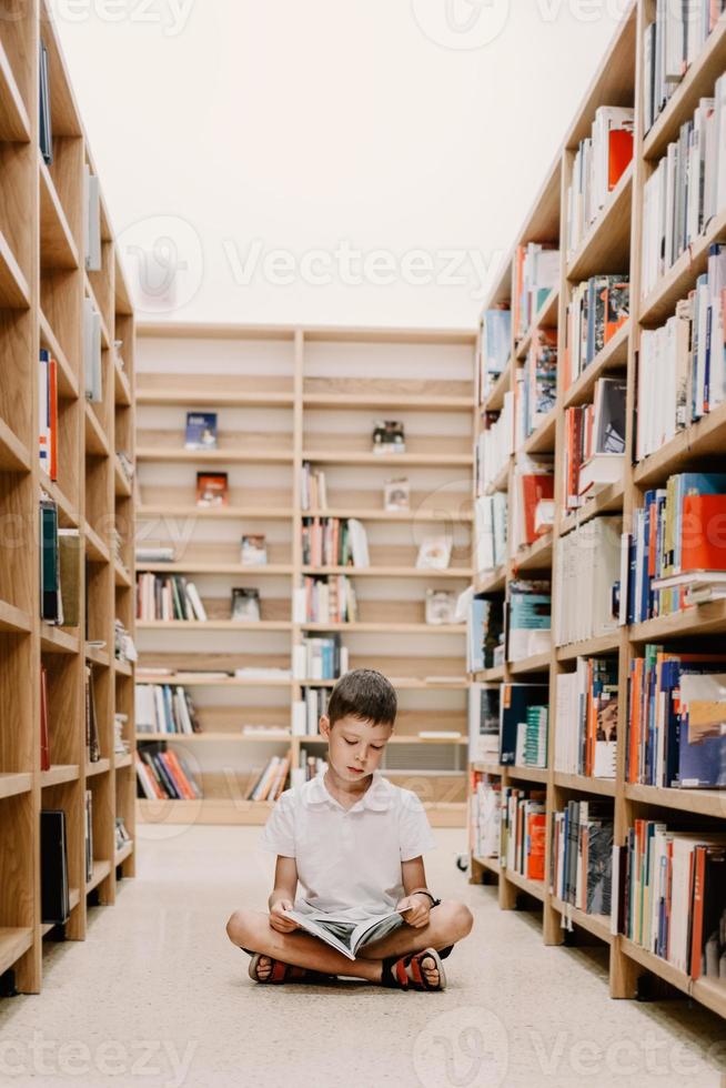 niño en la biblioteca de la escuela. los niños leen libros. niño leyendo y estudiando. niños en la librería. niño de preescolar inteligente inteligente que elige libros para pedir prestados. foto