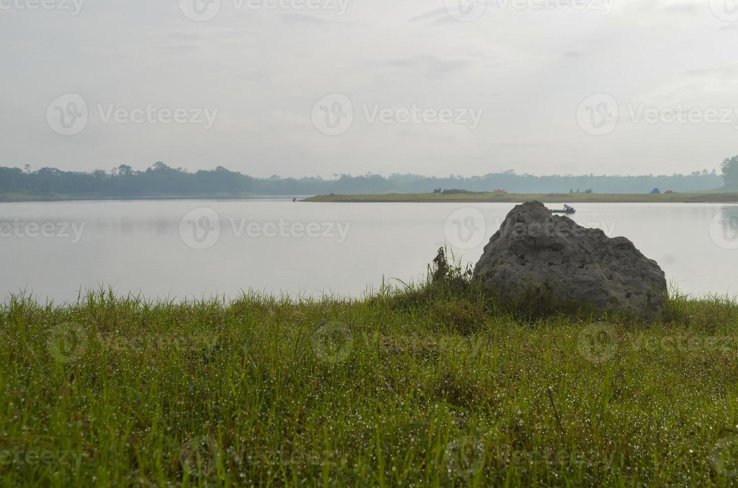Front view of reservoir Karangkates Malang Indonesia between mountains with foggy sky behind and a stone and meadows in the foreground photo