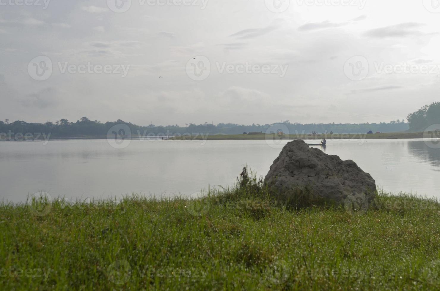 Front view of reservoir Karangkates Malang Indonesia between mountains with foggy sky behind and a stone and meadows in the foreground photo