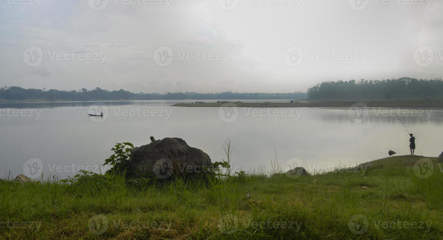Front view of reservoir Karangkates Malang Indonesia between mountains with foggy sky behind and a stone and meadows in the foreground photo