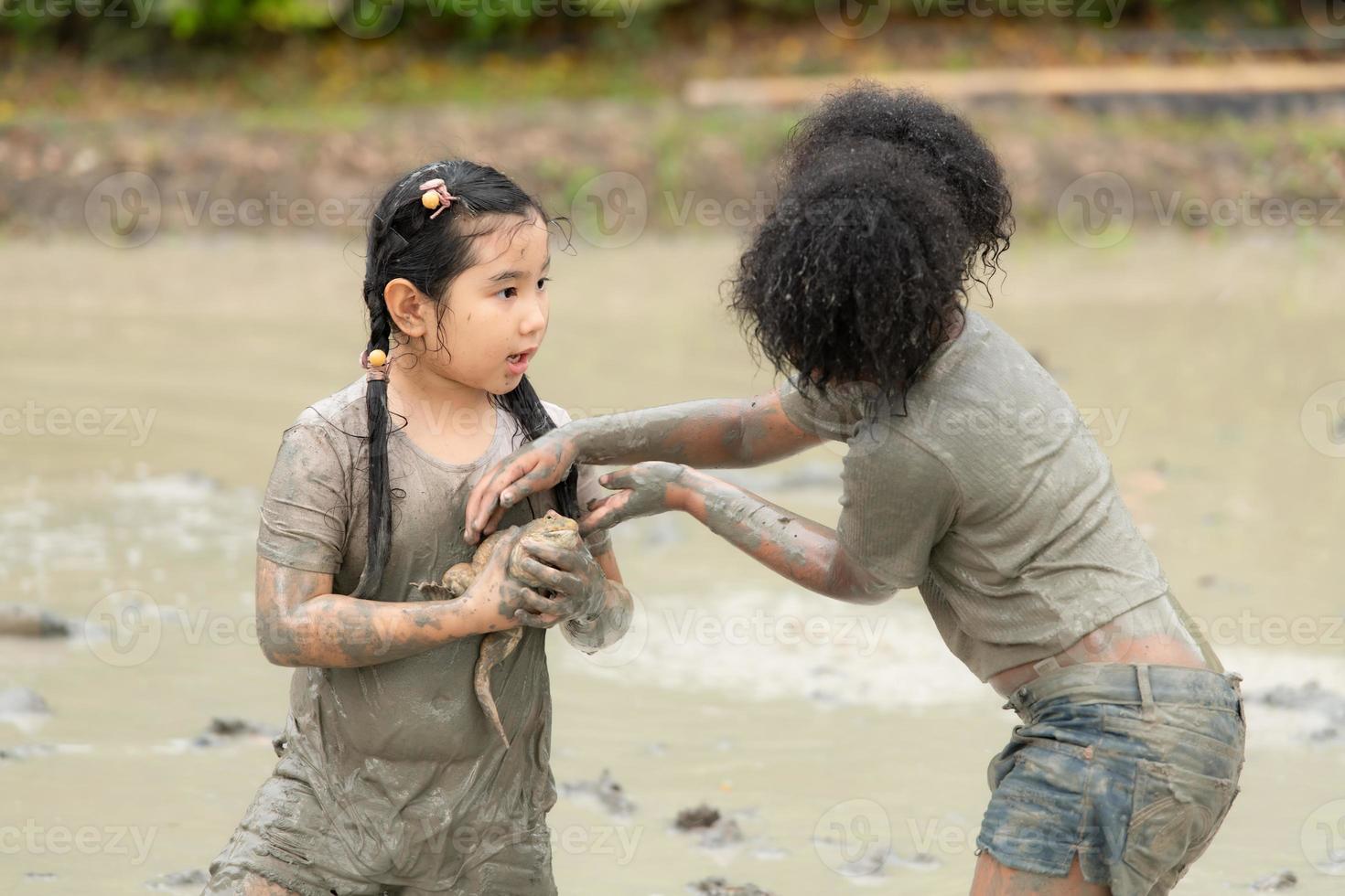 Children have fun playing in the mud in the community fields and catching a frog in a muddy field. photo