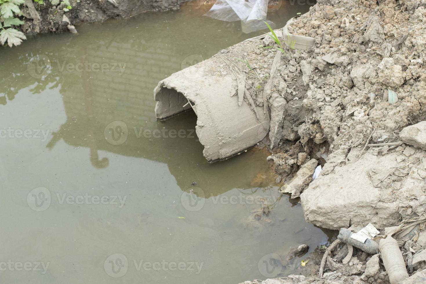 Waste draining. Pipe in ground. Old sewerage. Pipe goes into pond. Bad environment. photo